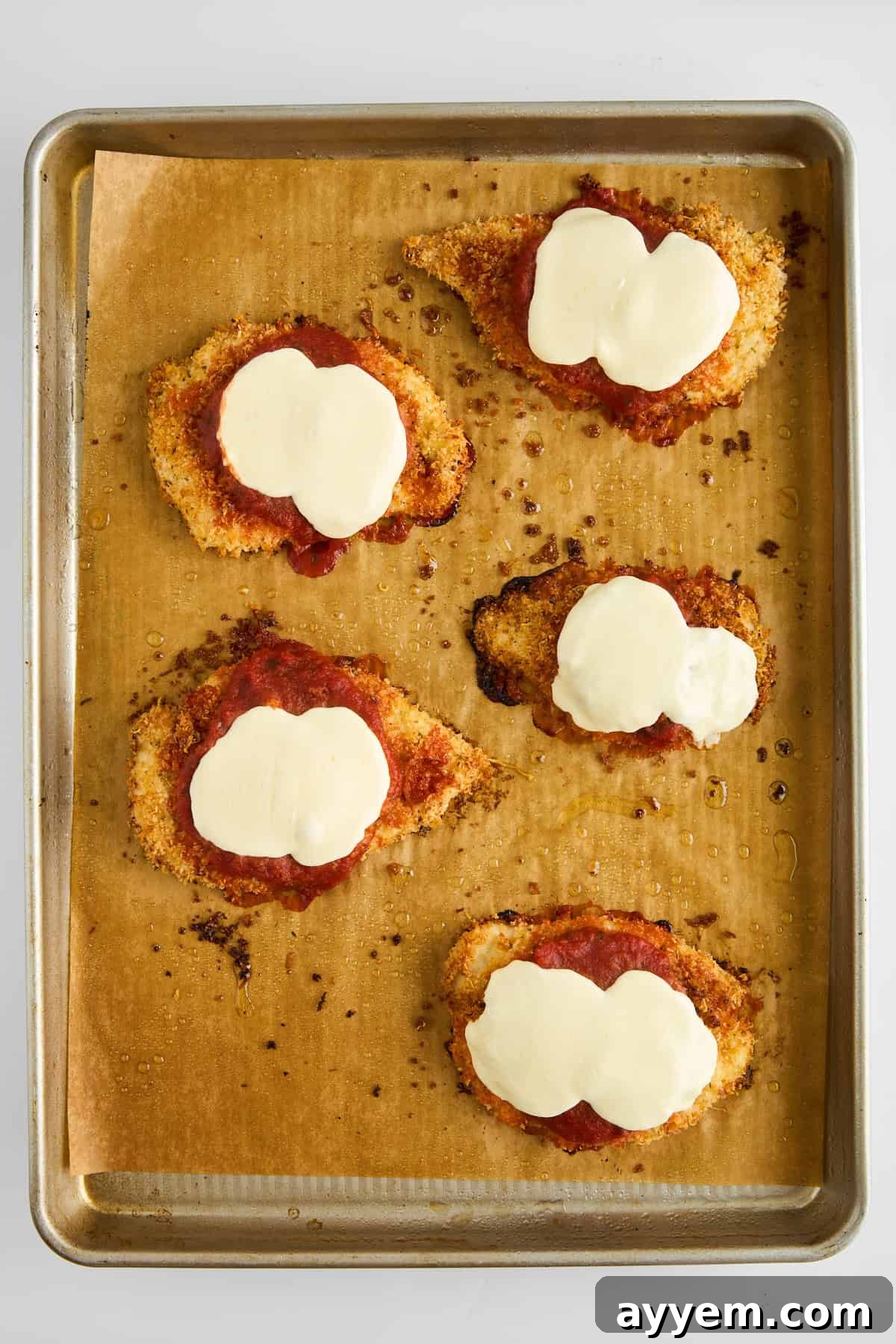 Five fully baked chicken parmesan pieces, with melted, bubbly cheese and golden crust, on a baking sheet.