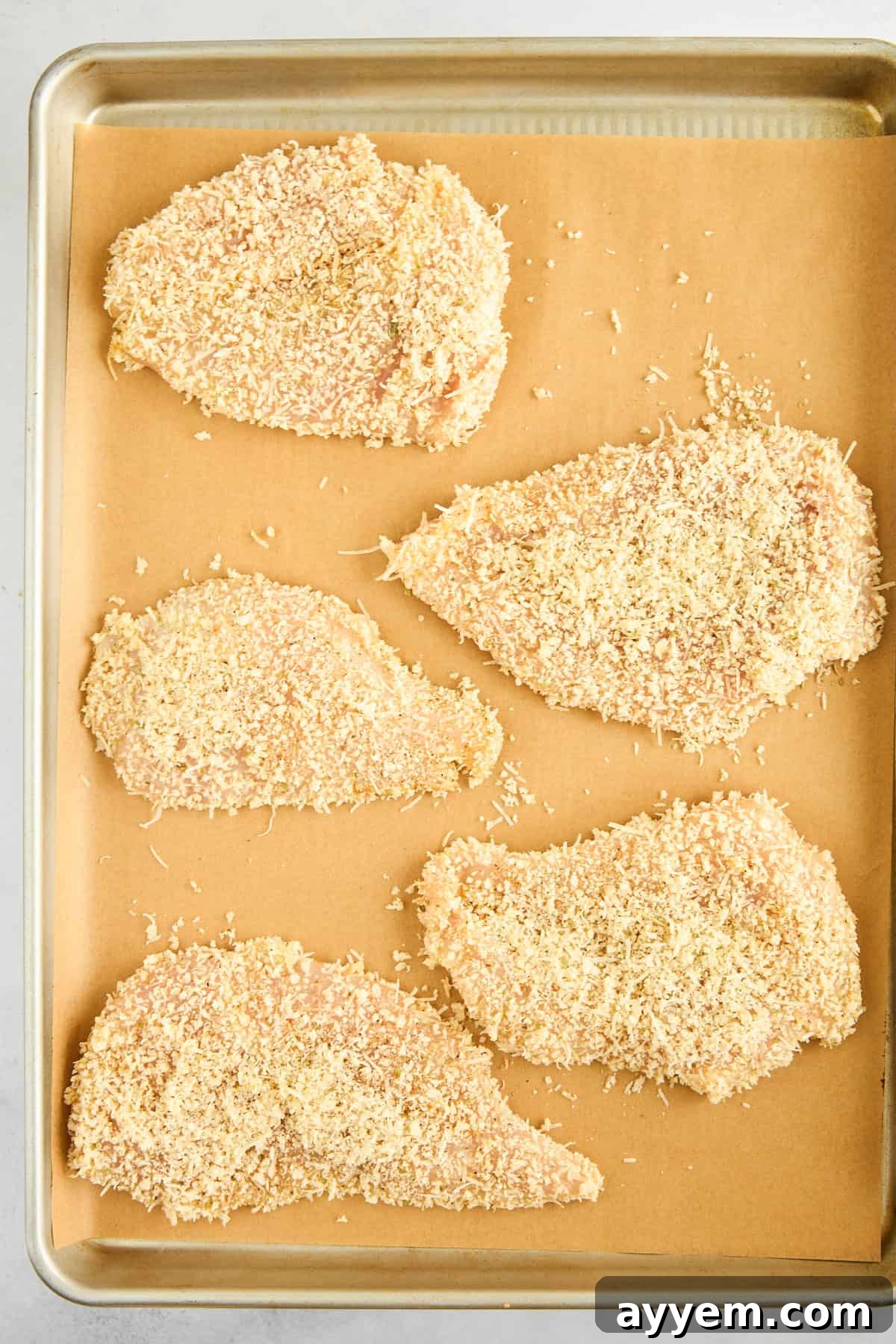 Raw breaded chicken pieces perfectly arranged on a baking sheet.