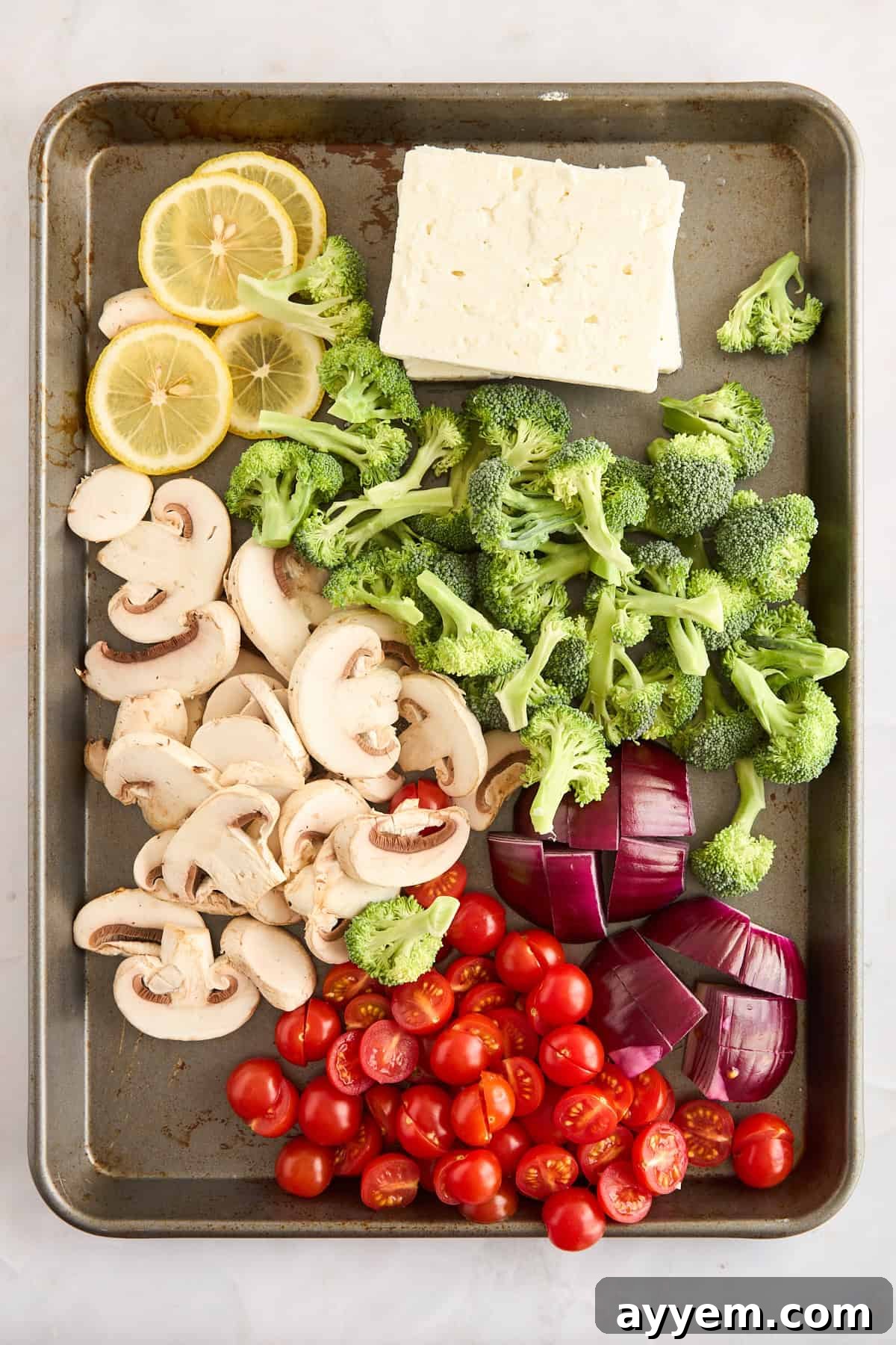Raw vegetables and blocks of feta cheese arranged on a baking sheet, ready for seasoning.
