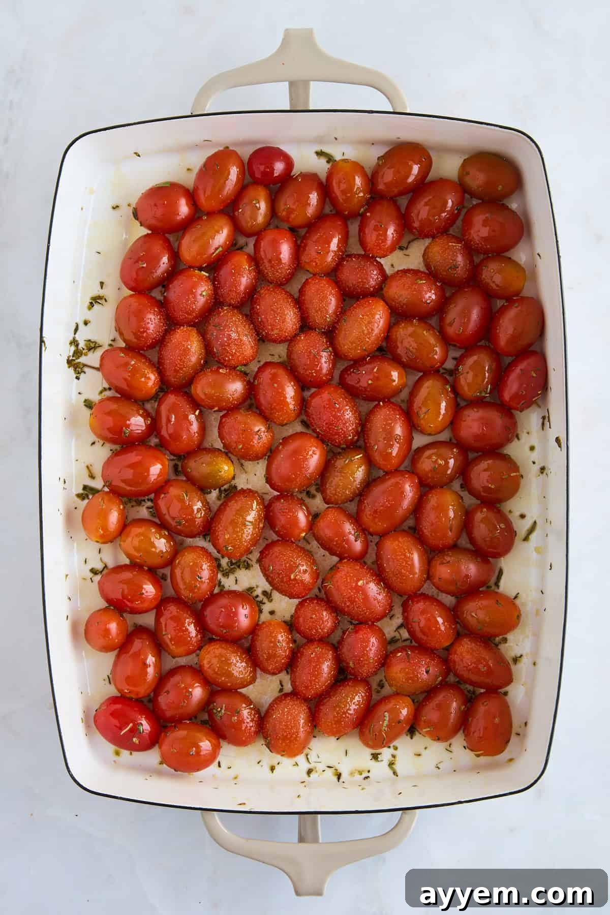 Cherry tomatoes seasoned with olive oil, salt, and pepper in a baking dish, ready for roasting.