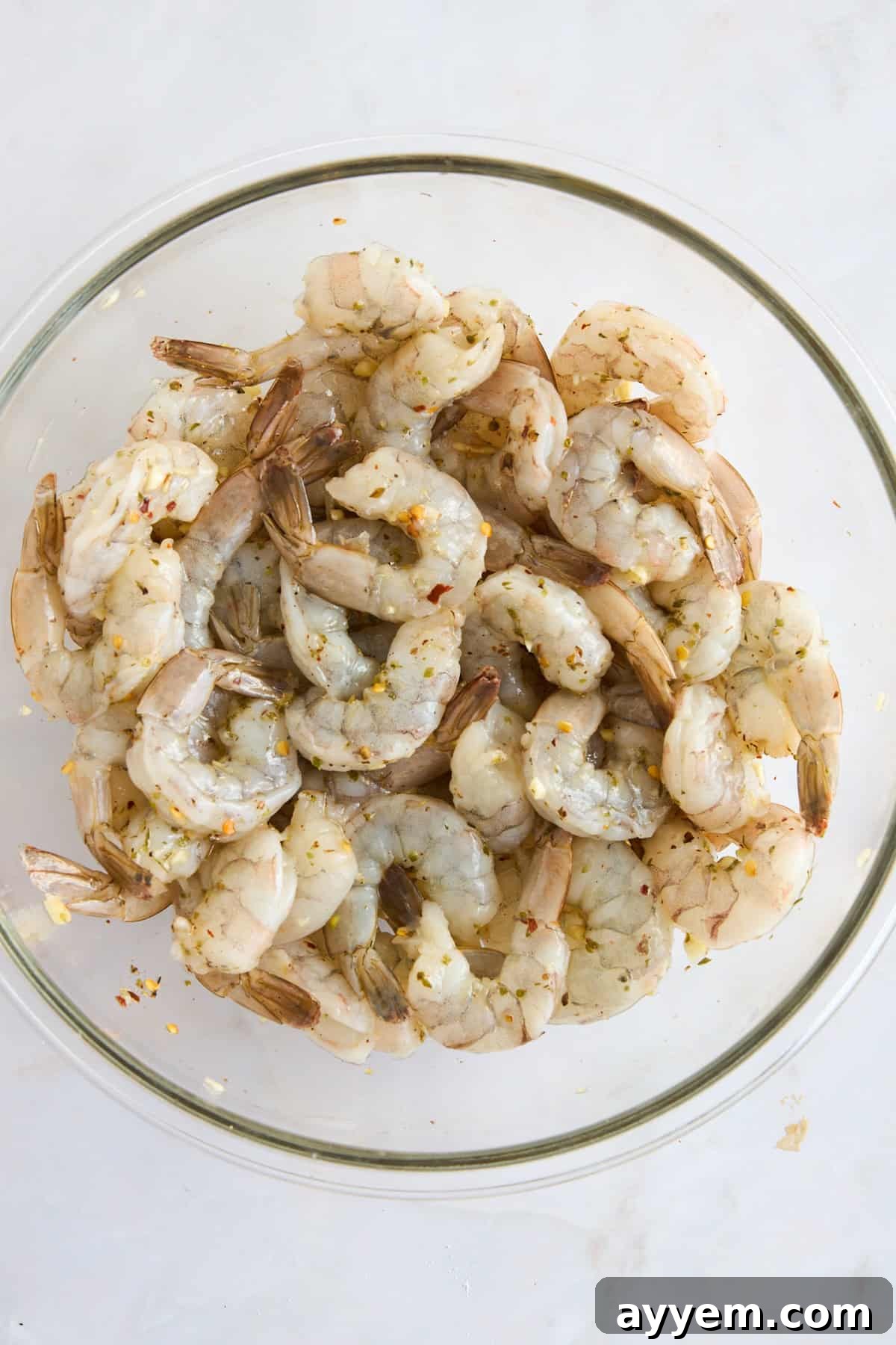 Raw shrimp in a bowl coated with olive oil and seasonings. 