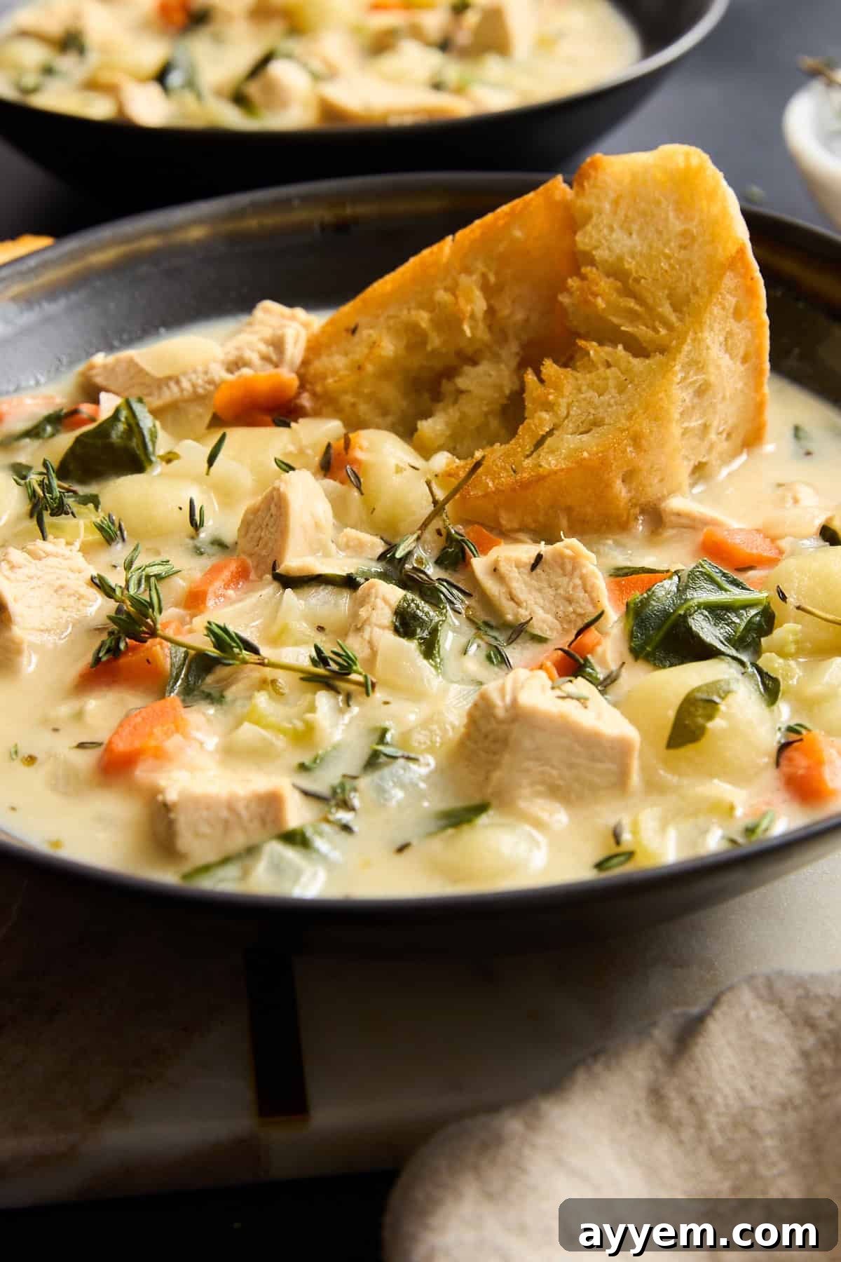 A perfectly served bowl of Olive Garden chicken gnocchi soup, garnished with parsley and a side of bread.
