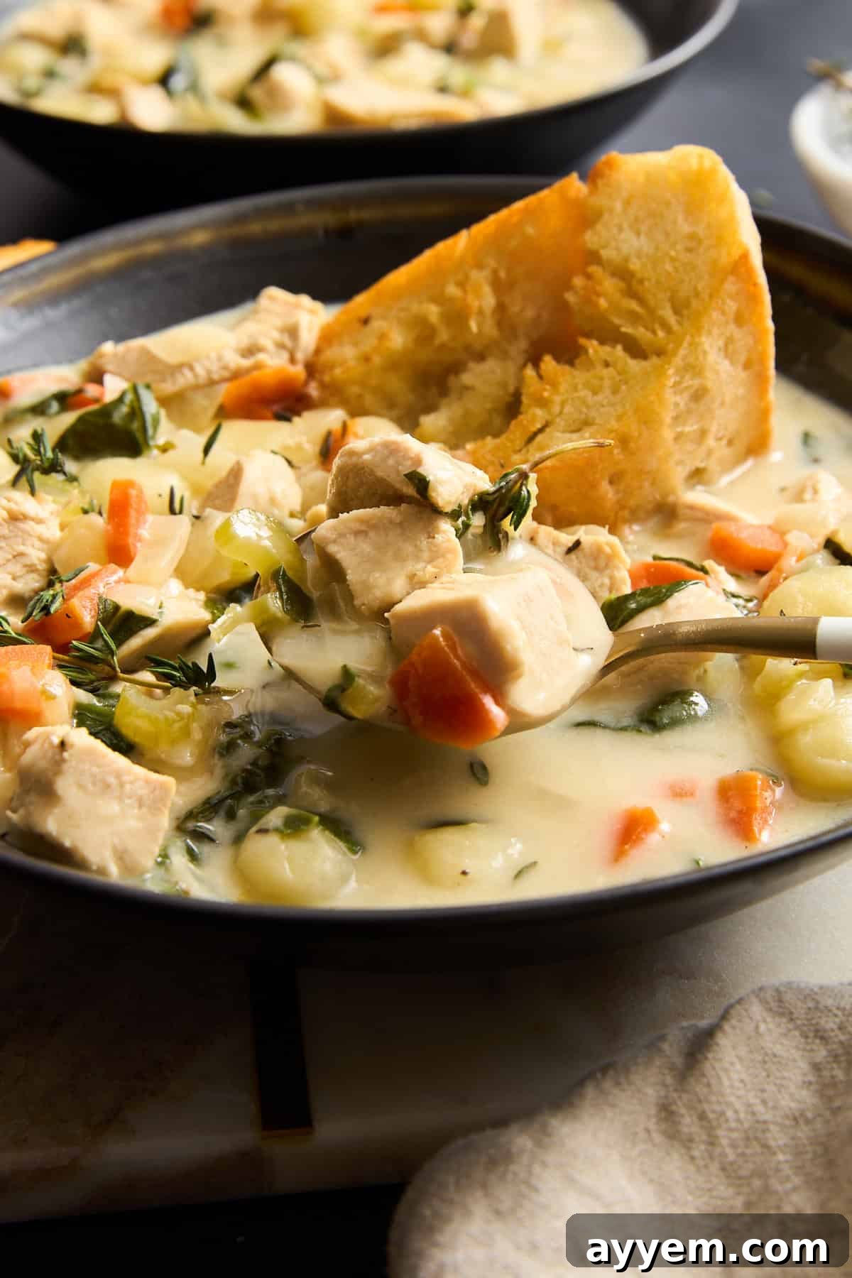 A spoon lifting a scoop of chicken and gnocchi soup from a bowl.