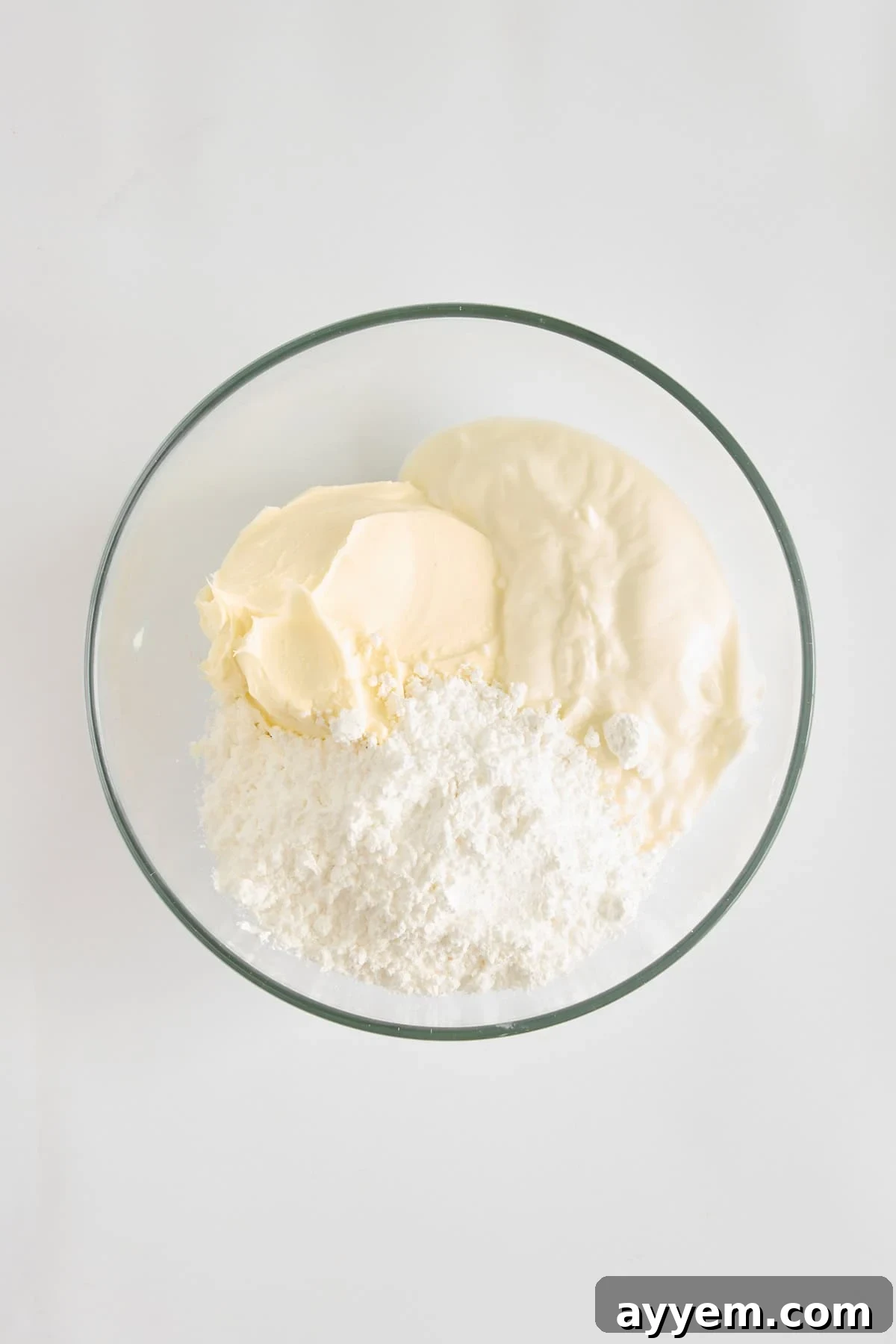 Powdered sugar, mascarpone cheese, and Greek yogurt in a mixing bowl, ready to be blended for the creamy dressing.