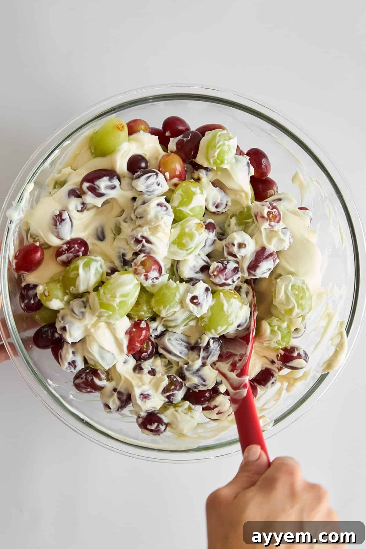 Grape salad being gently combined in a large bowl, showcasing the creamy dressing coating the colorful grapes.