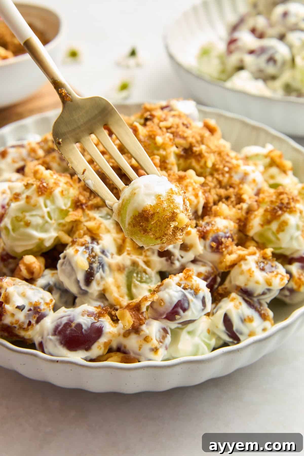 A fork holding a perfect bite of Mediterranean-inspired grape salad, showcasing the creamy coating and walnut topping.