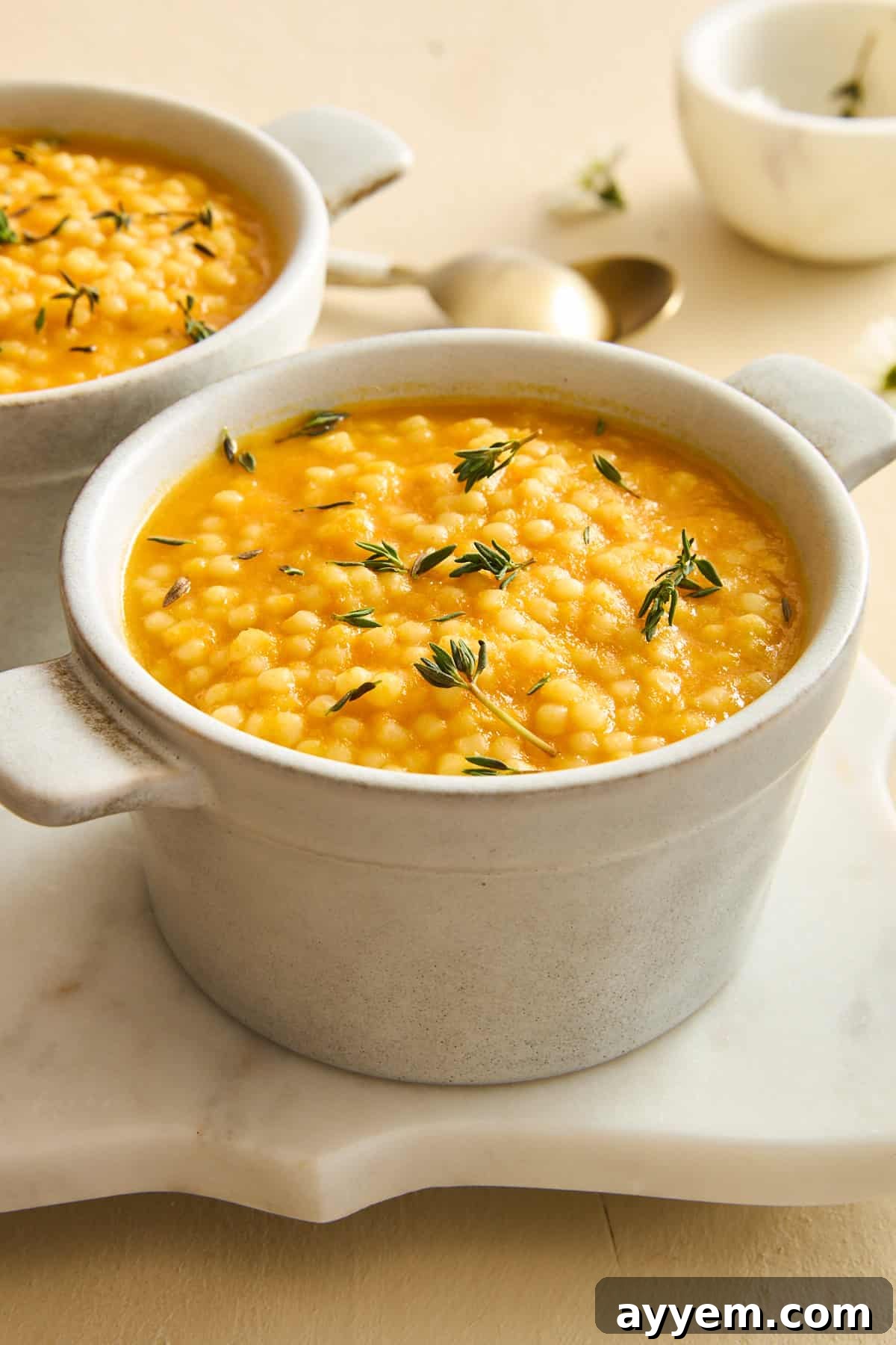 A ramekin of pastina soup topped with fresh rosemary, ready to be served.