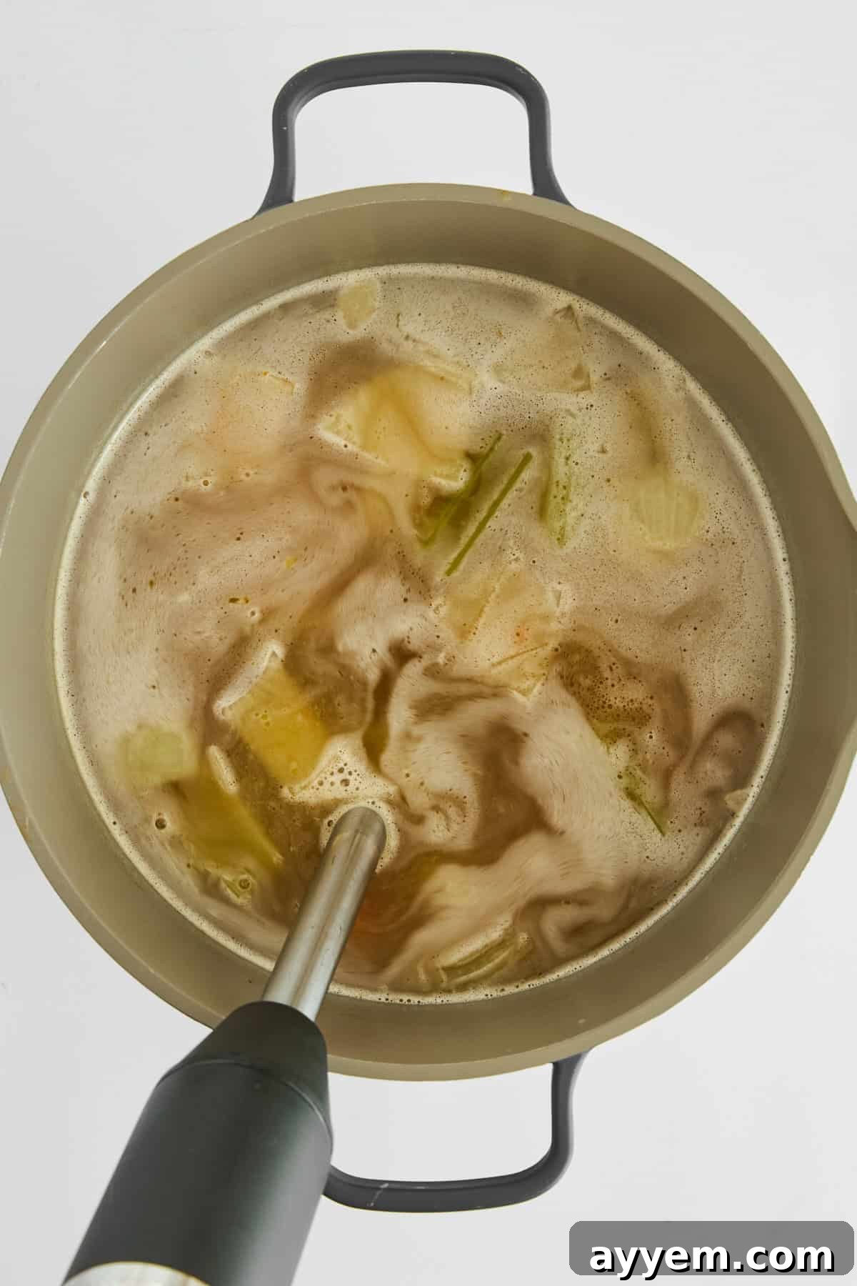 An immersion blender smoothly combining tender vegetables into a rich broth directly in the pot, creating a silky base for pastina soup.