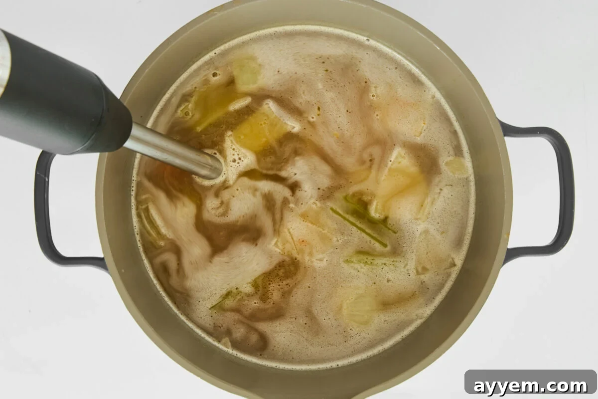 An immersion blender blending vegetables in a pot of broth.