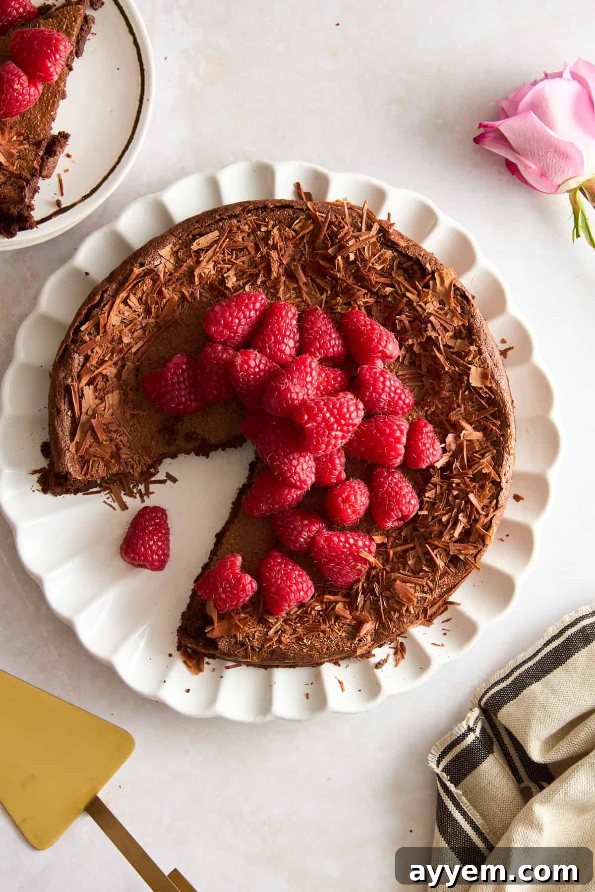 A beautifully presented flourless chocolate cake, adorned with vibrant fresh raspberries, with a single slice perfectly removed to reveal its dense, fudgy interior.