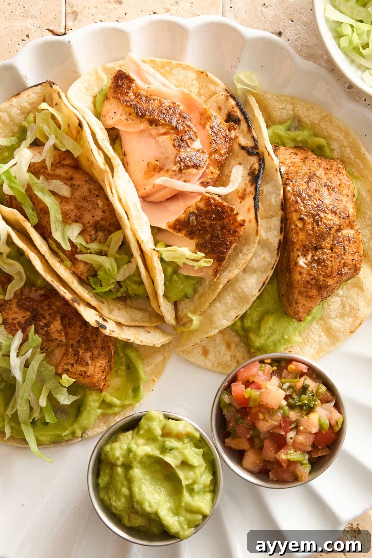 A plate of four salmon tacos with guacamole and pico de gallo, presented beautifully.