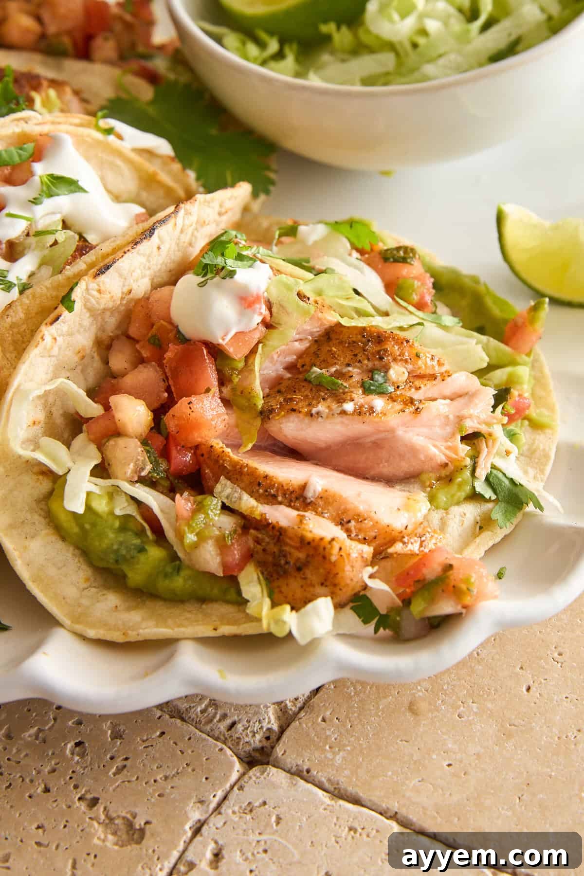 A single salmon taco, garnished with fresh lettuce, creamy guacamole, and vibrant pico de gallo.