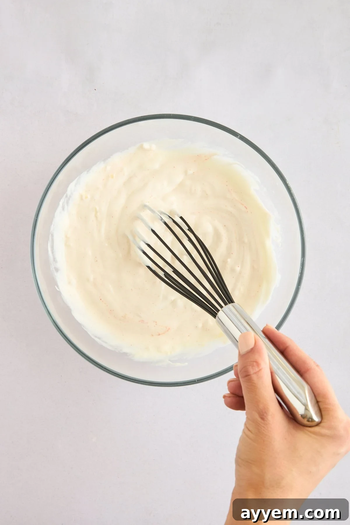 Garlic yogurt sauce being whisked to achieve a smooth consistency.