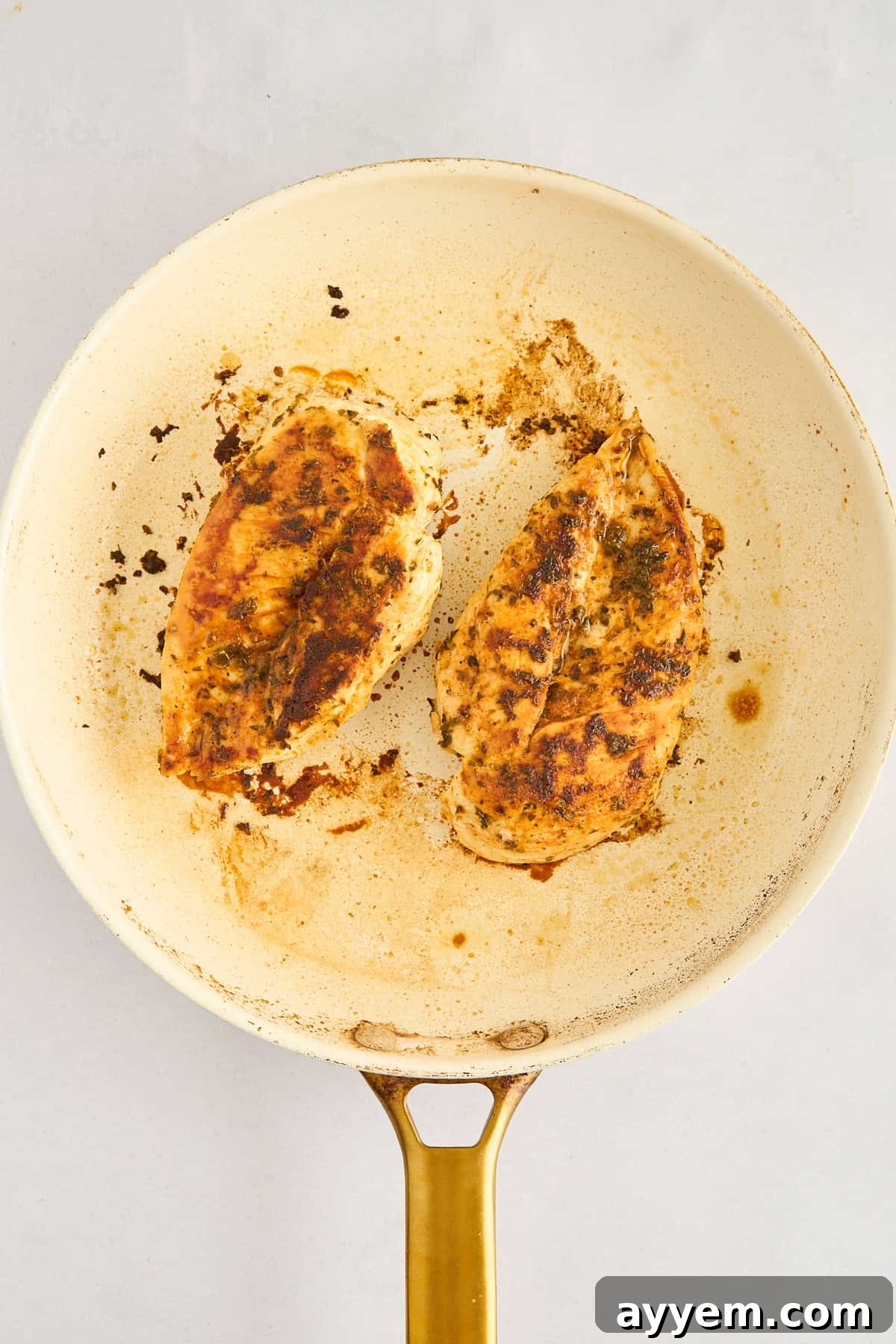 Two boneless, skinless chicken breasts searing in a hot skillet with olive oil.