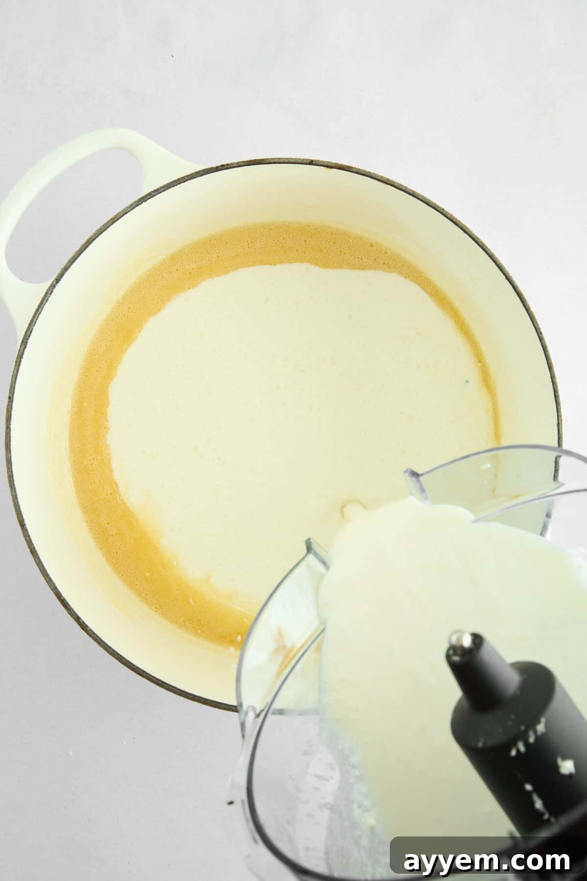 Smooth, blended cottage cheese mixture being poured into a pot of melted butter and flour to create the sauce.