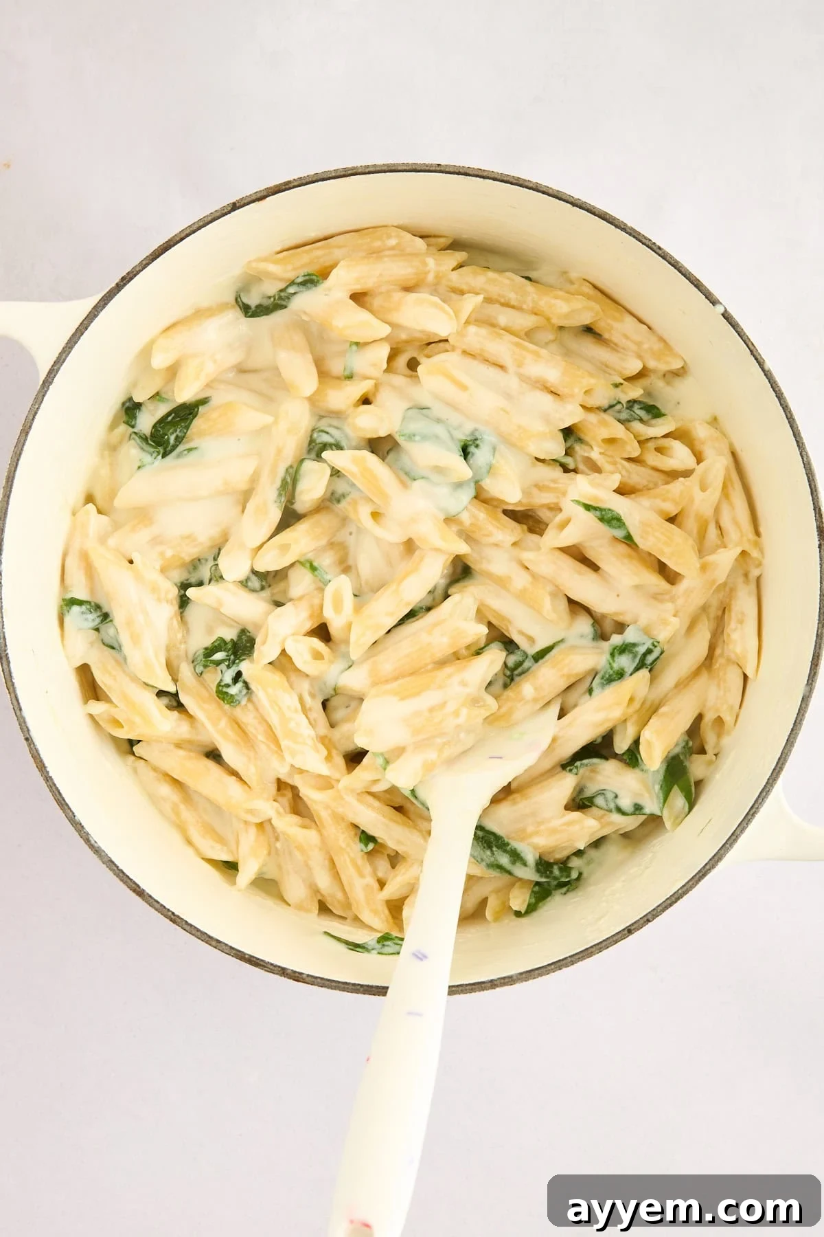 Penne pasta being tossed with creamy cottage cheese sauce and fresh spinach in a large pot.