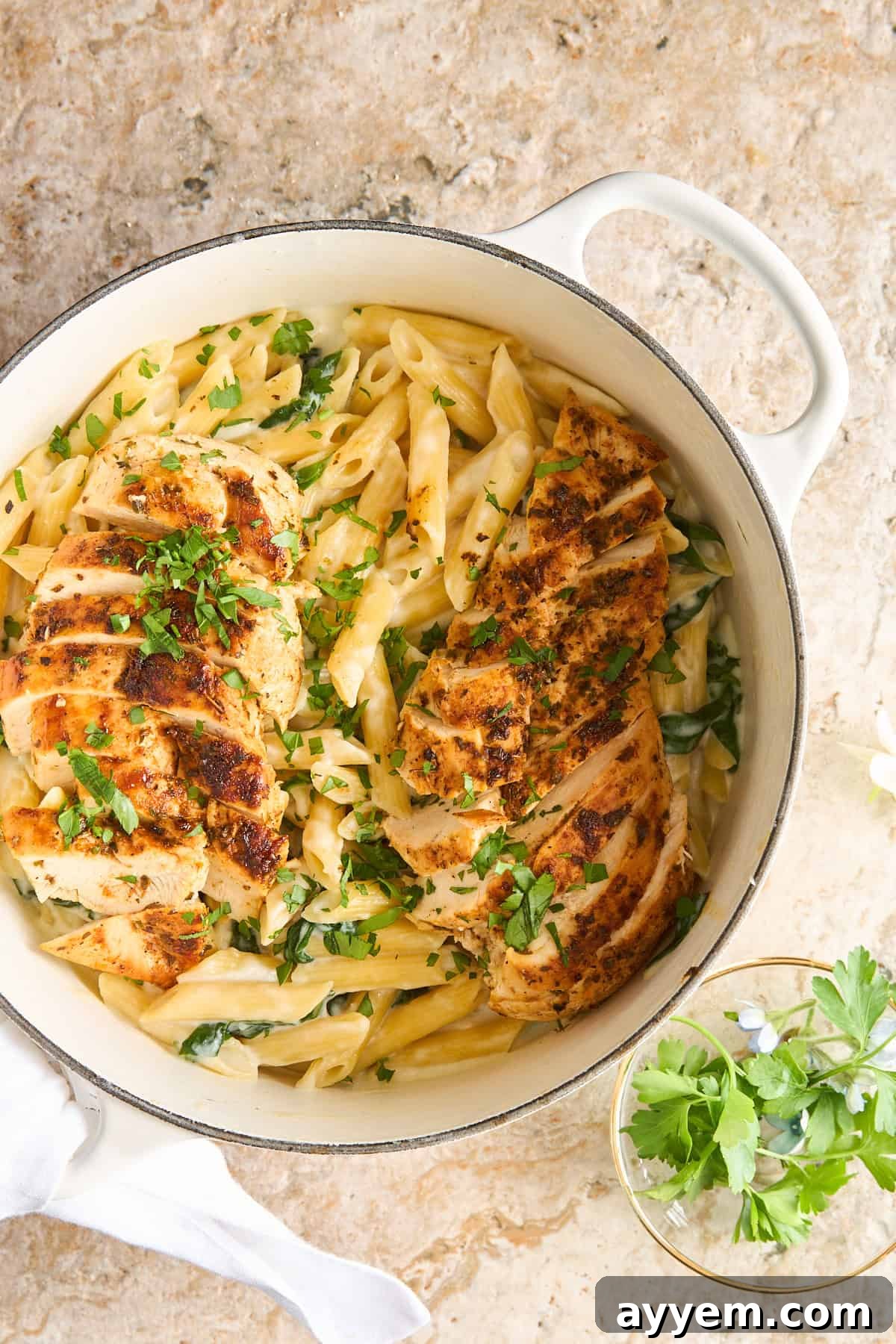 A pot of creamy cottage cheese pasta with spinach, topped with sliced grilled chicken and garnished with fresh herbs.