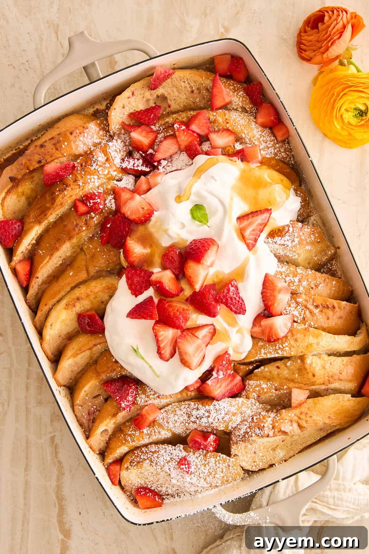 A baking dish of strawberry french toast topped with whipped cream and strawberries, ready for serving.