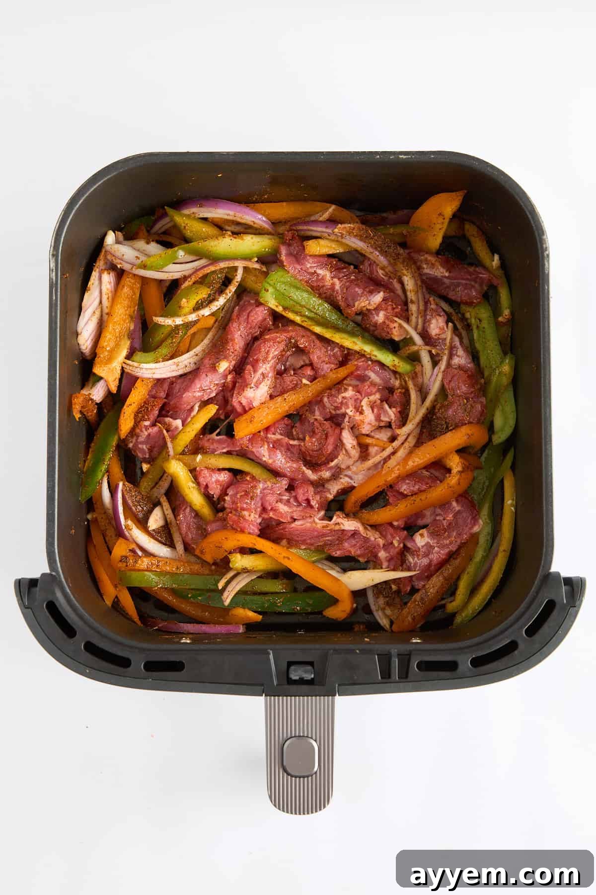 Raw steak strips, bell peppers, and onions seasoned and ready for the air fryer.