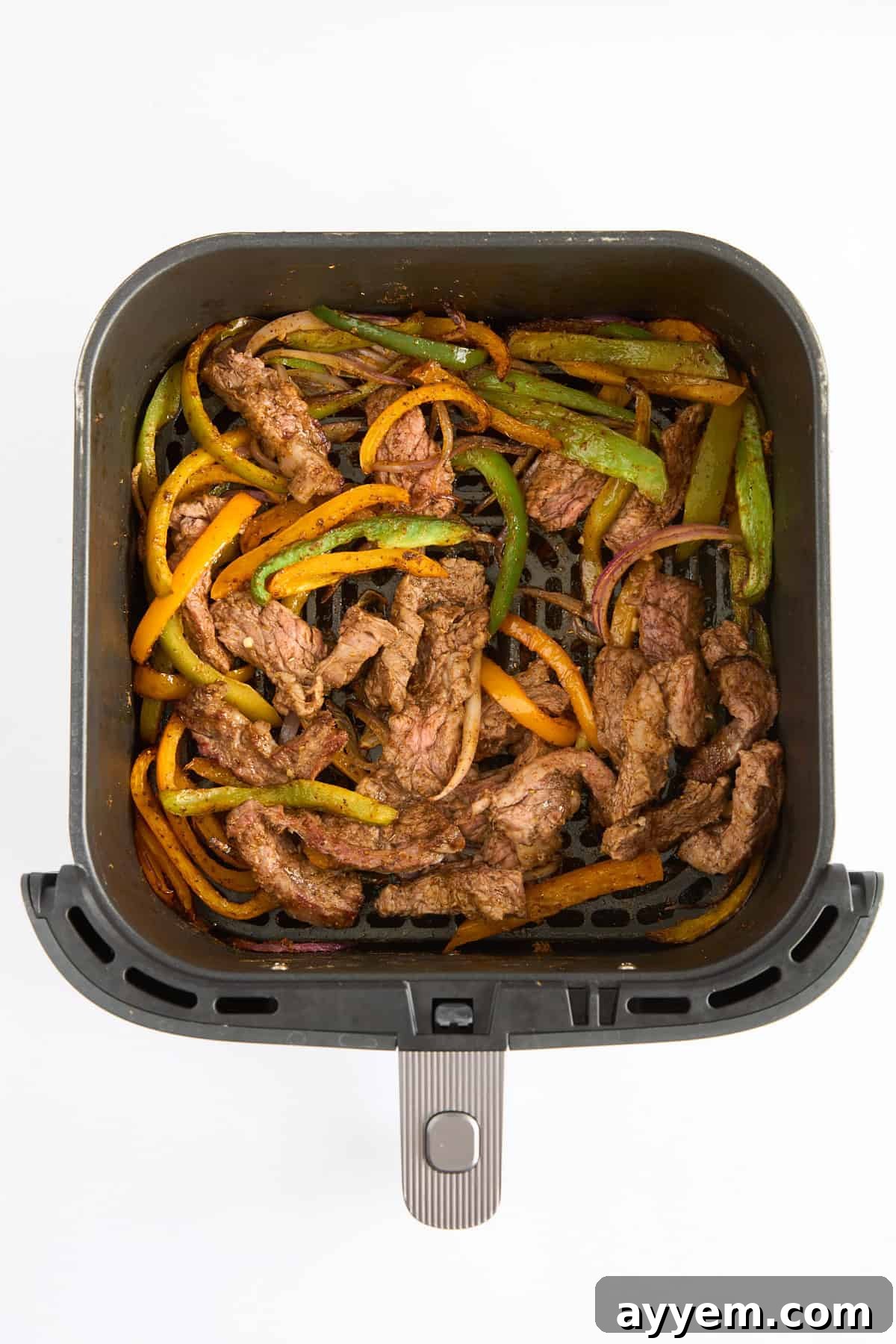 Perfectly cooked steak fajitas in an air fryer basket, steam rising.