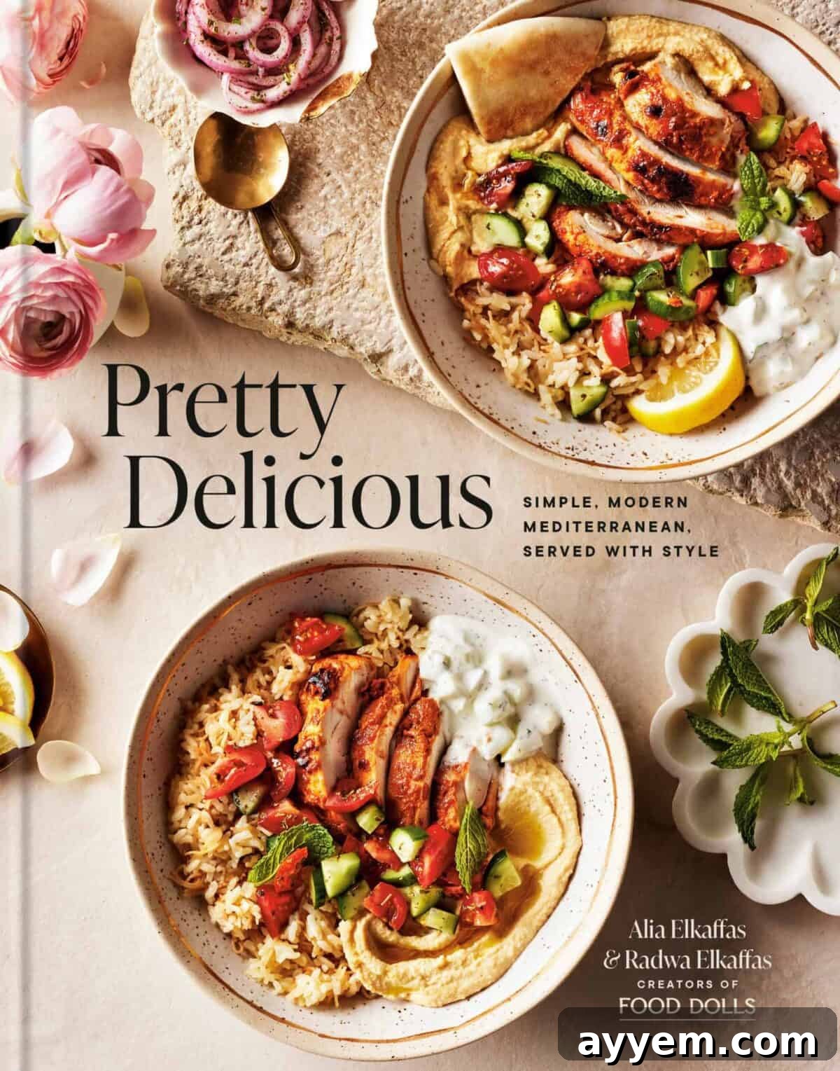 Crafting the Perfect Influencer Box: Our Secrets Revealed 2 A cookbook titled Pretty Delicious featuring Mediterranean dishes. The cover shows two bowls with rice, grilled vegetables, falafel, and pita, garnished with lemon and herbs. Pink flowers and a small dish with yogurt are nearby.
