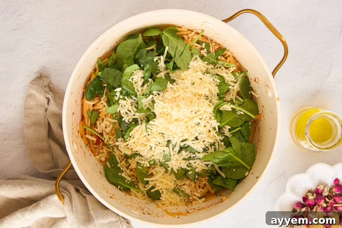 Spinach and parmesan cheese being added to a pot of cooked pasta.