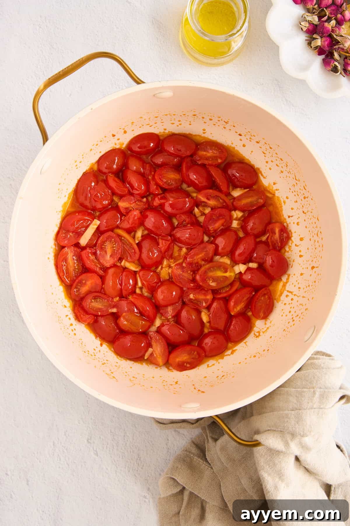 Sautéing halved grape tomatoes and minced garlic in olive oil within a pasta pot, showing the softening and release of juices.