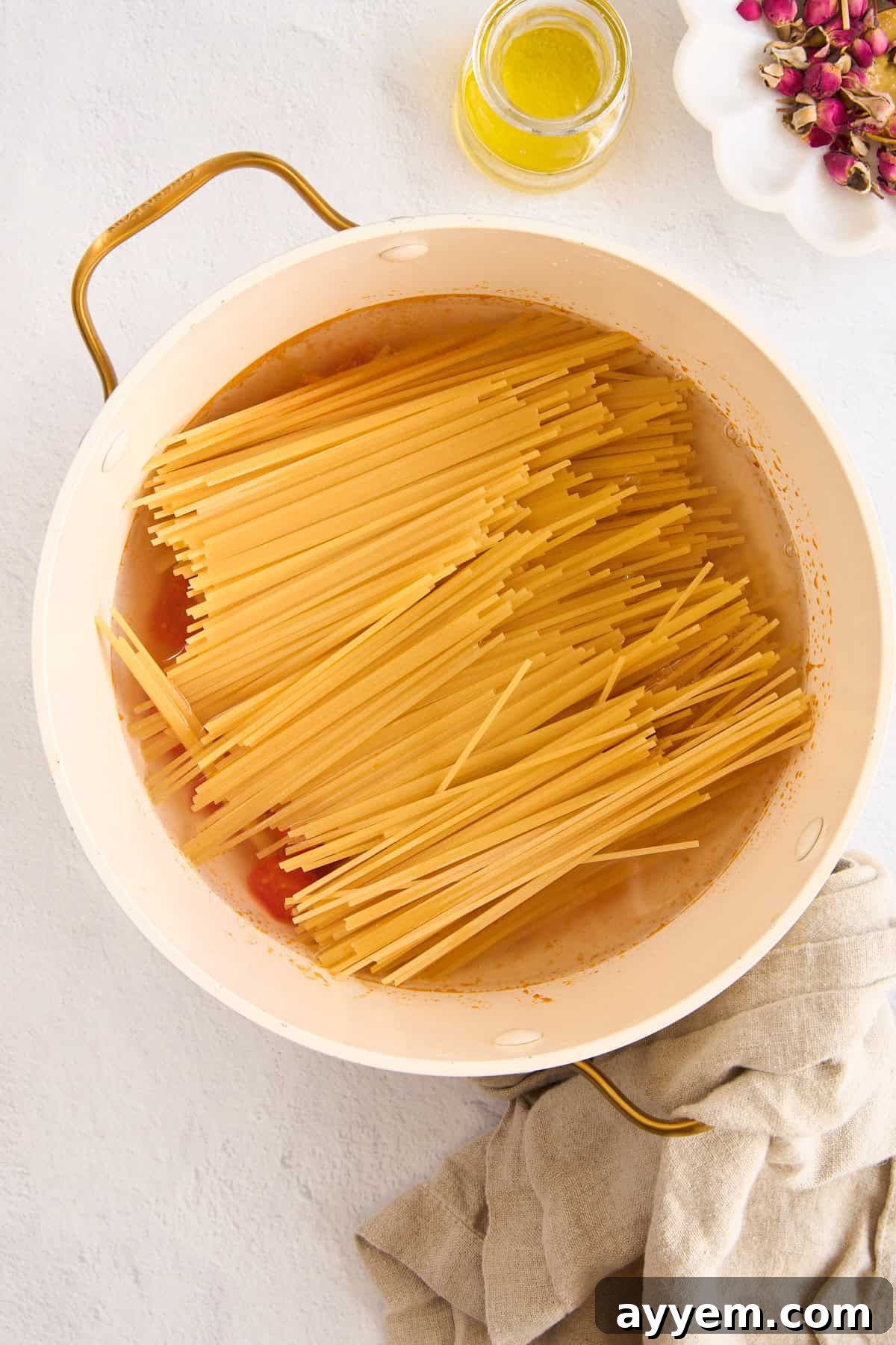 Uncooked spaghetti noodles arranged on top of the sautéed tomatoes and garlic in a large pot, awaiting the addition of boiling water.
