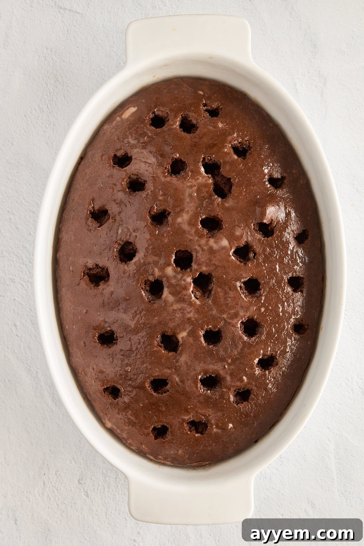 Chocolate milk being poured over the poked cake.