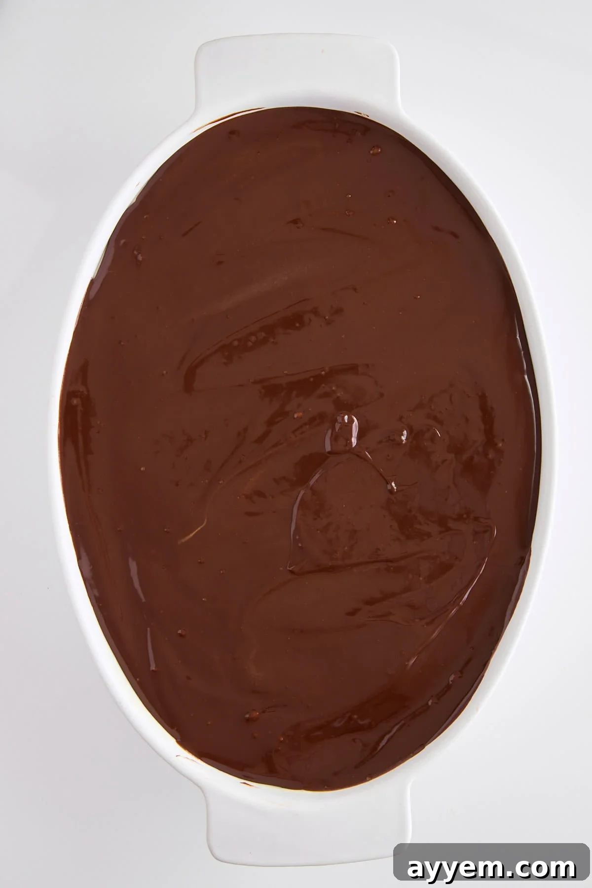 Smooth chocolate ganache being poured over the creamy layer.