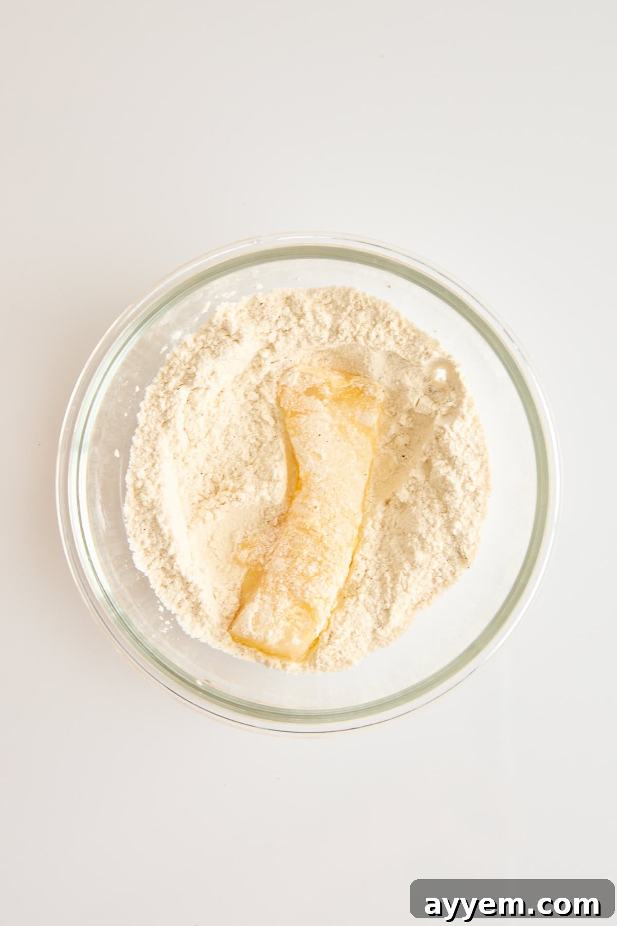 An egg-dipped cod piece in a bowl of flour, ready for the next coating step.