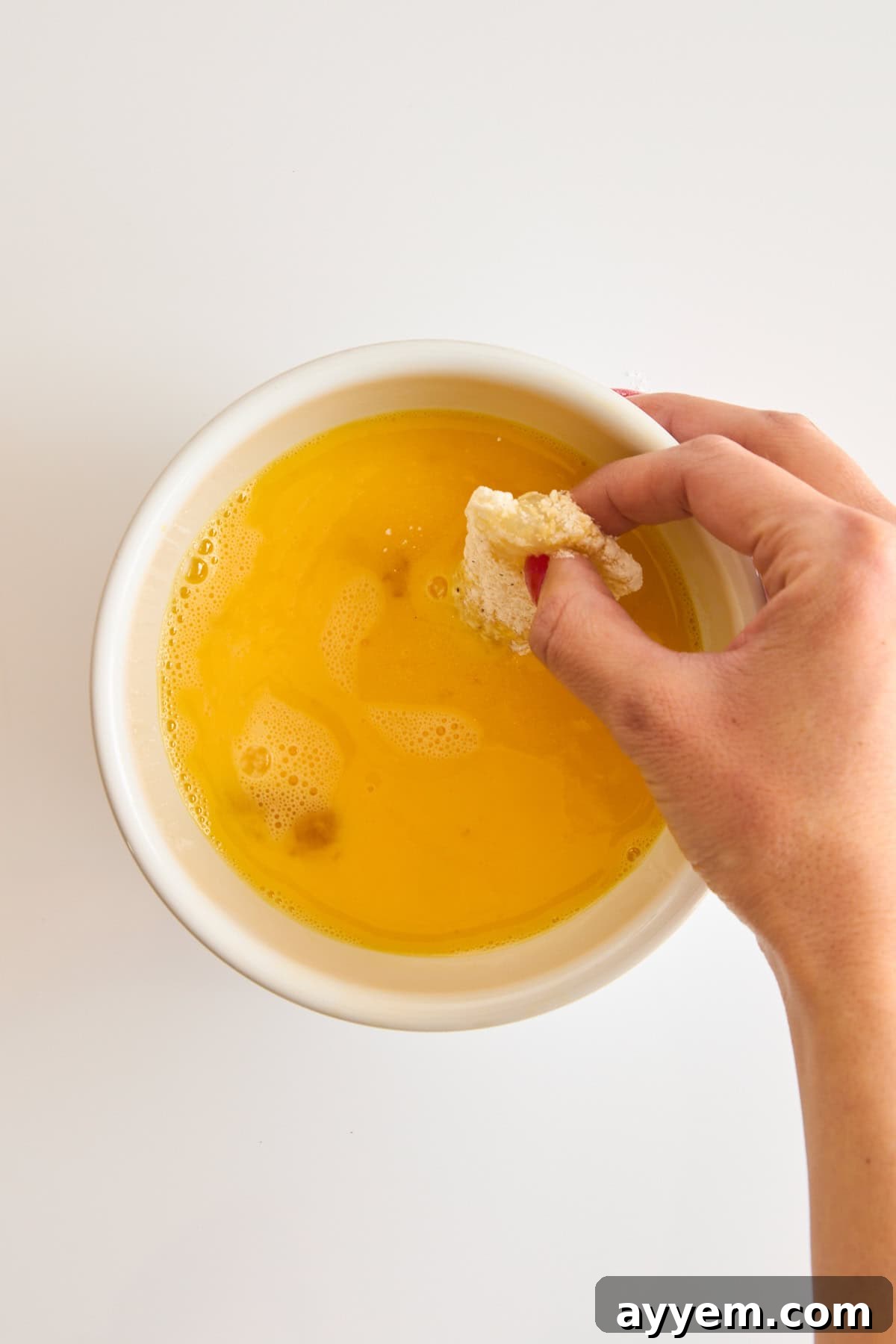A flour-coated cod piece being dipped back into a bowl of whisked egg for double breading.