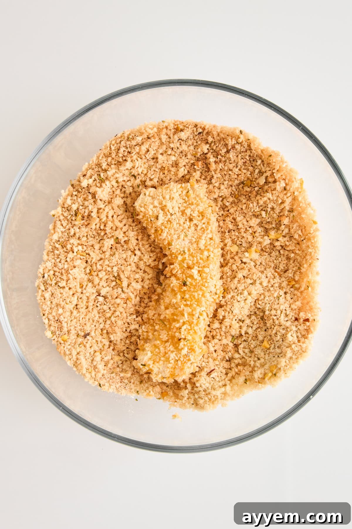 A fully coated cod piece in a bowl of panko breadcrumbs, ready for frying.