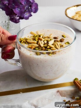 A hand holding a mug of sahlab topped with crushed nuts.