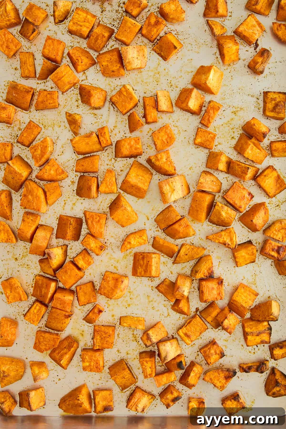Freshly cubed sweet potatoes seasoned with olive oil and spices, spread evenly on a baking sheet, ready for roasting to achieve perfect caramelization and tenderness.