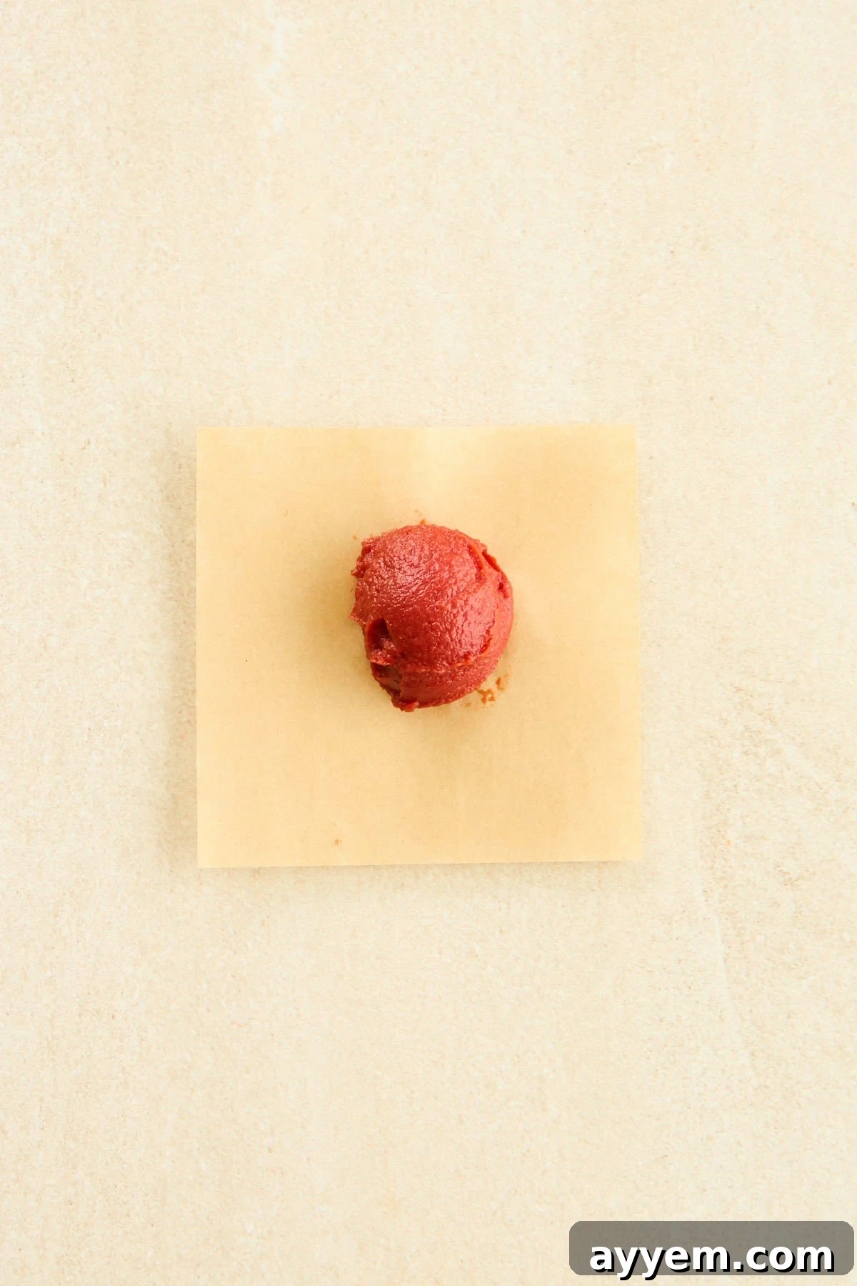 A tablespoon of rich red tomato paste resting on a square of parchment paper, ready for freezing.