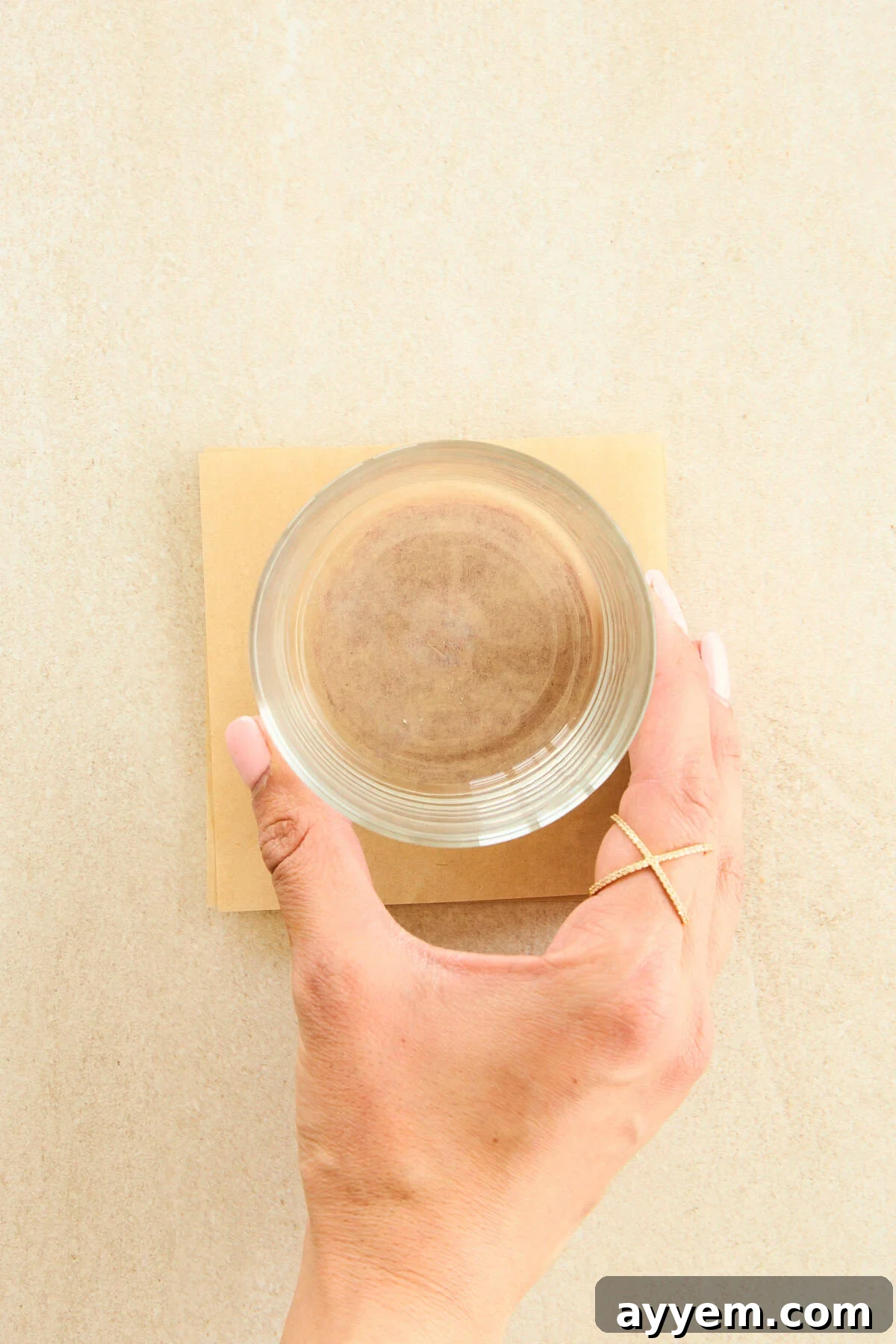 A cup being used to gently flatten a scoop of tomato paste between two sheets of parchment paper.