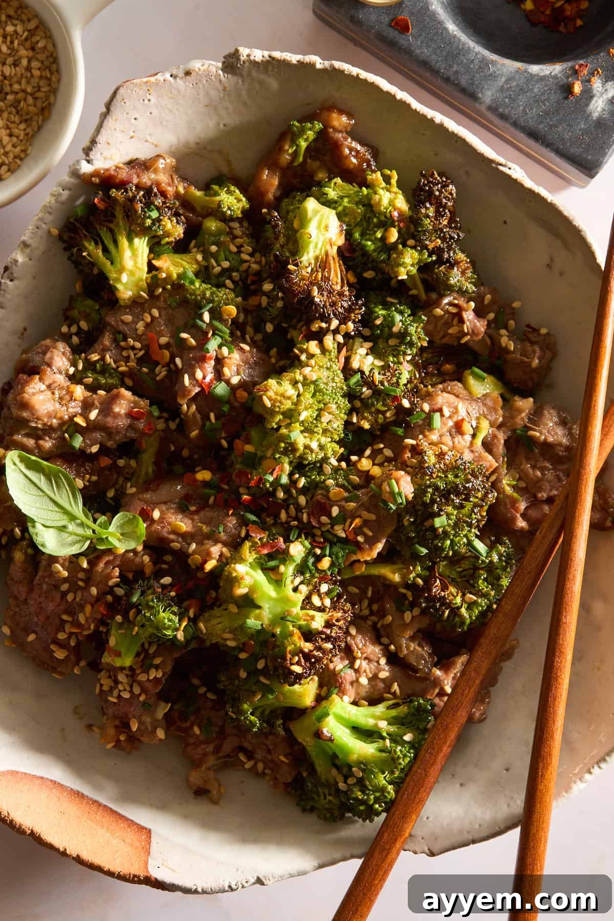 A bowl of air fryer beef and broccoli with chopsticks balanced on the side. 