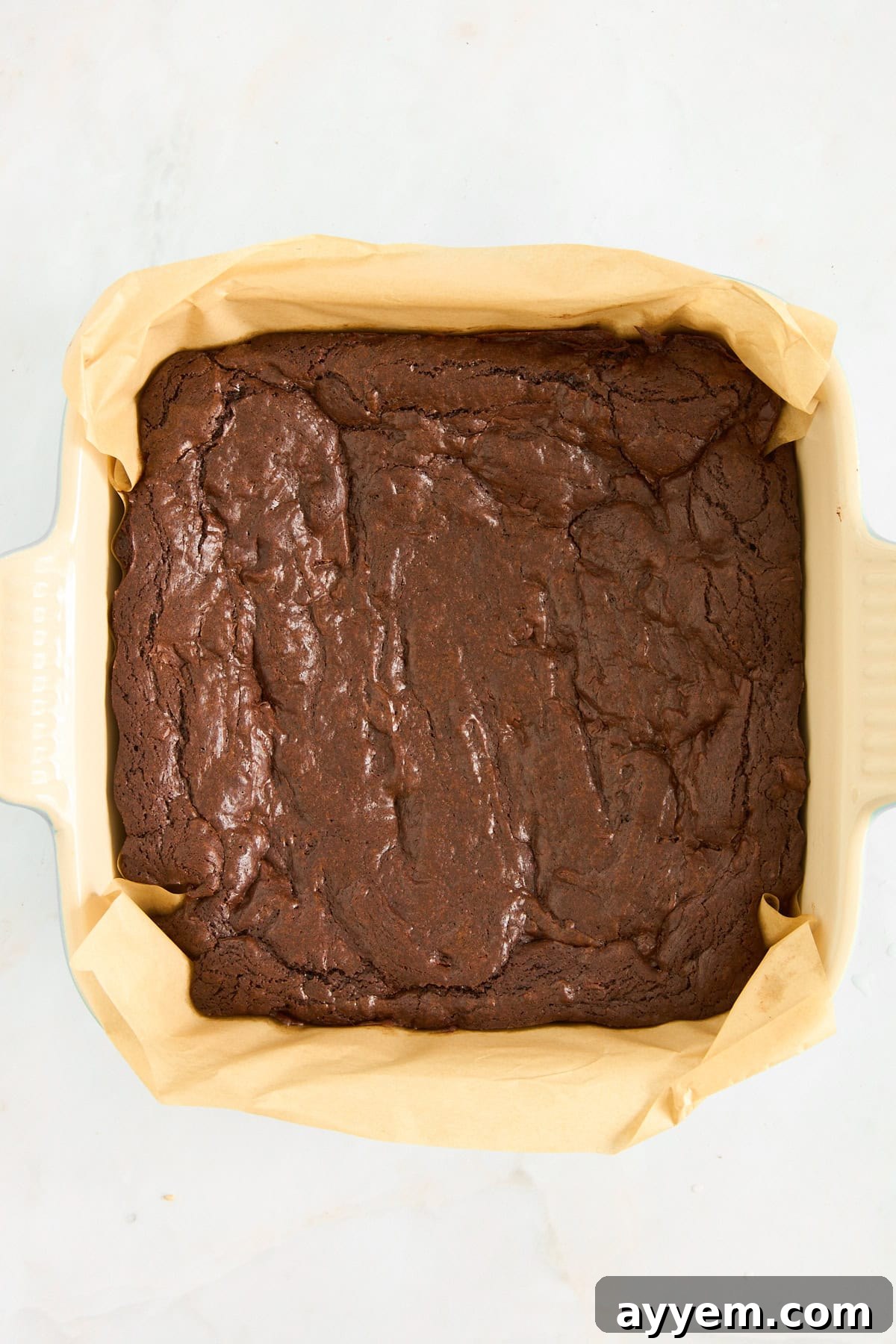 Freshly baked chocolate brownies cooling in a parchment paper-lined baking dish, ready for their mascarpone topping.
