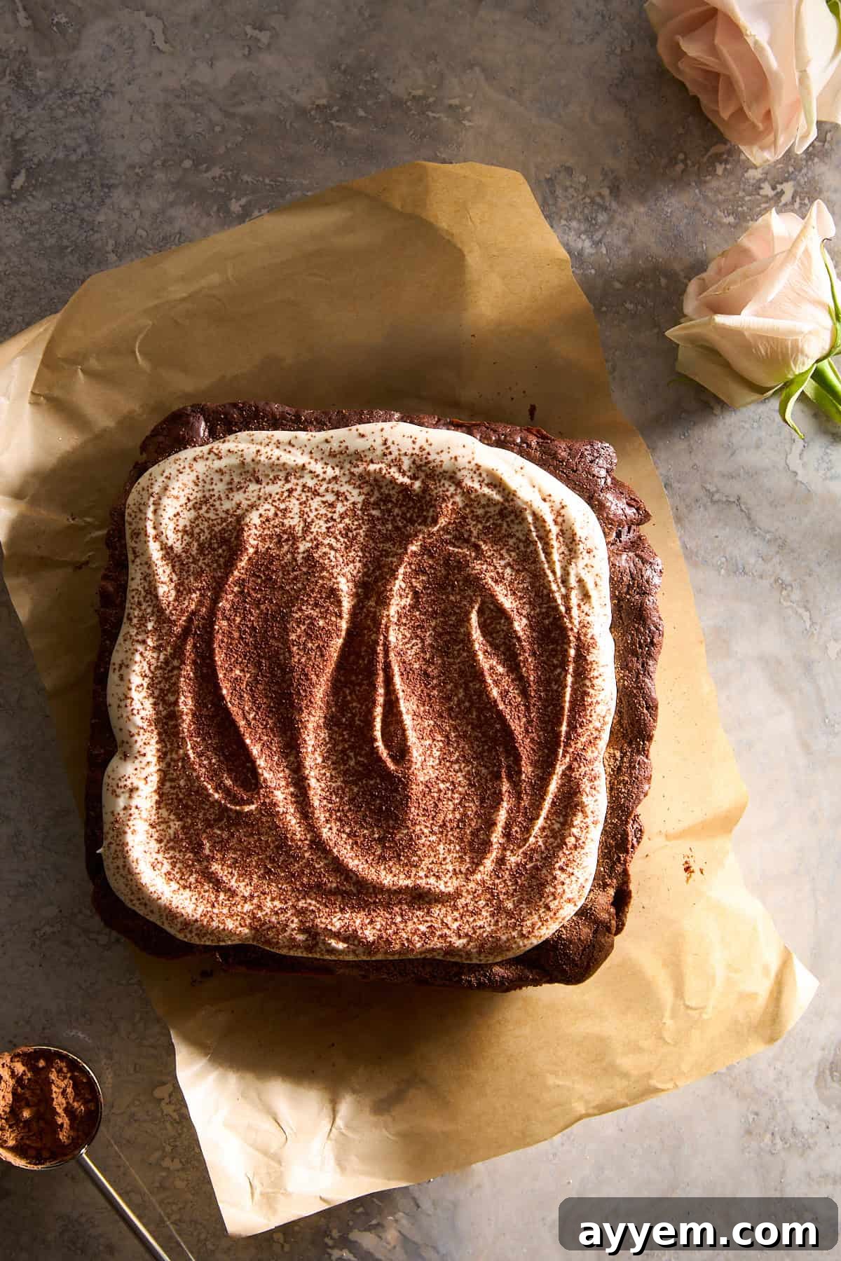 Close-up of Tiramisu Brownies in a pan, generously topped with fluffy mascarpone cream and dusted with cocoa powder, ready to be sliced.