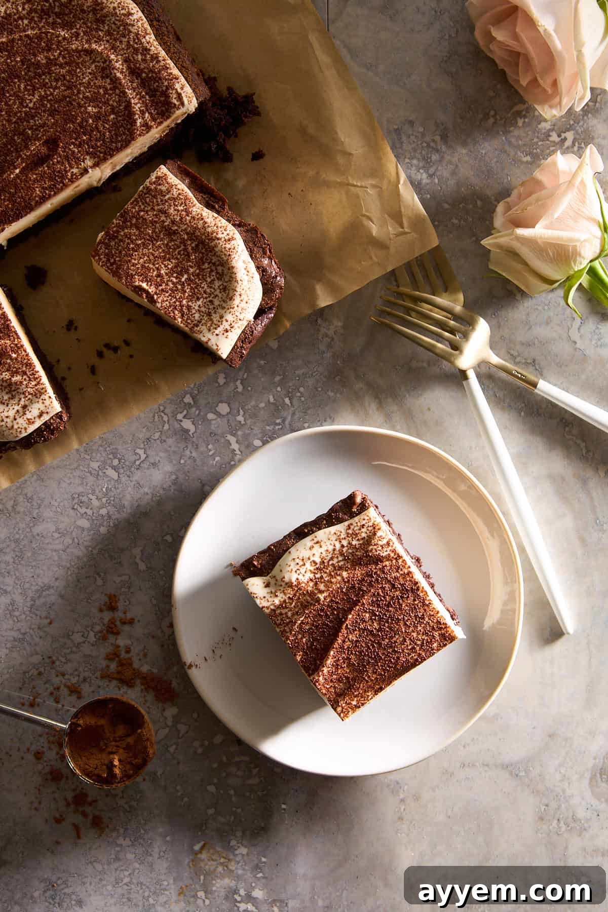 A single Tiramisu Brownie slice on a plate next to a larger slab of unsliced brownies, highlighting the distinct layers of brownie and mascarpone.