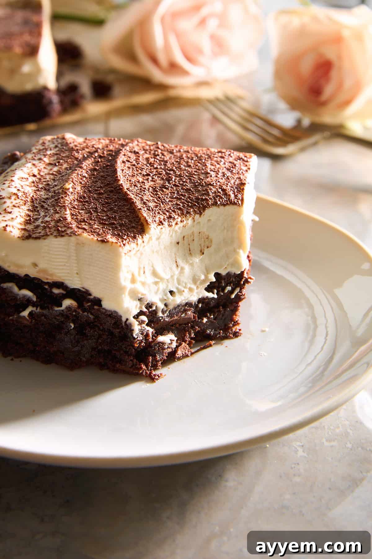 A tiramisu brownie slice on a plate with a corner bite missing.