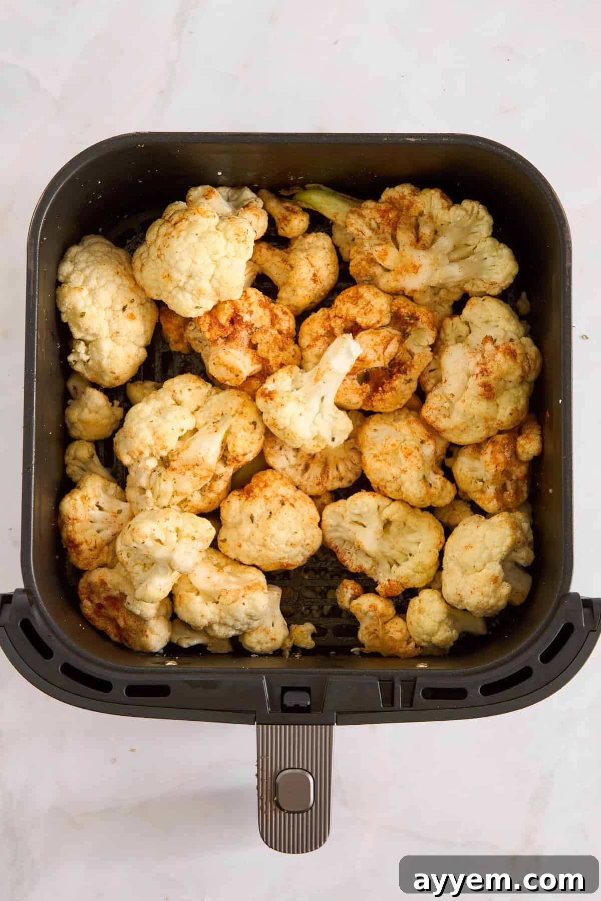 Raw, seasoned cauliflower florets in an air fryer basket, ready for cooking.