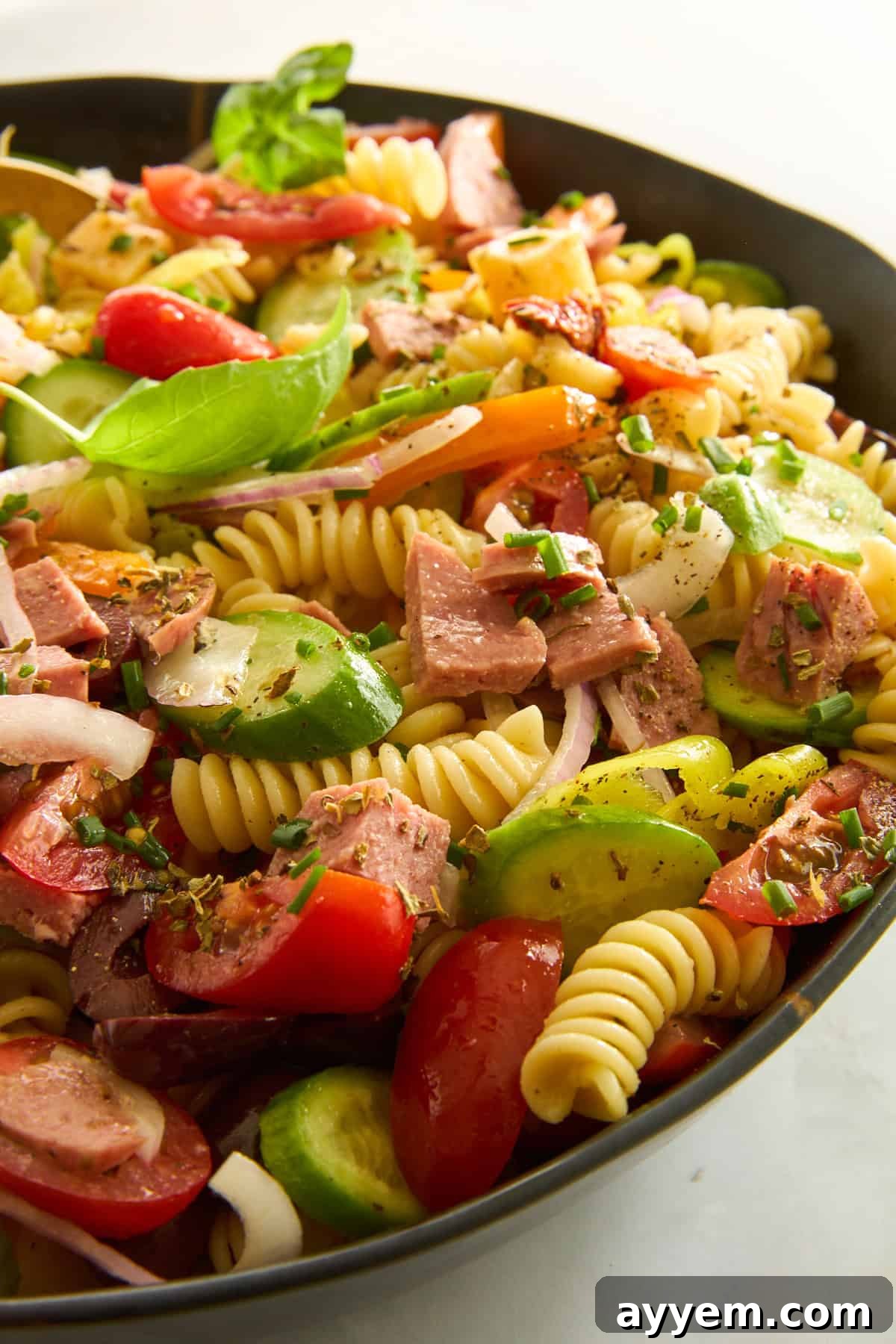 A close-up shot of Mediterranean pasta salad in a bowl, highlighting the cubed salami, fresh vegetables, and pasta coated in dressing.