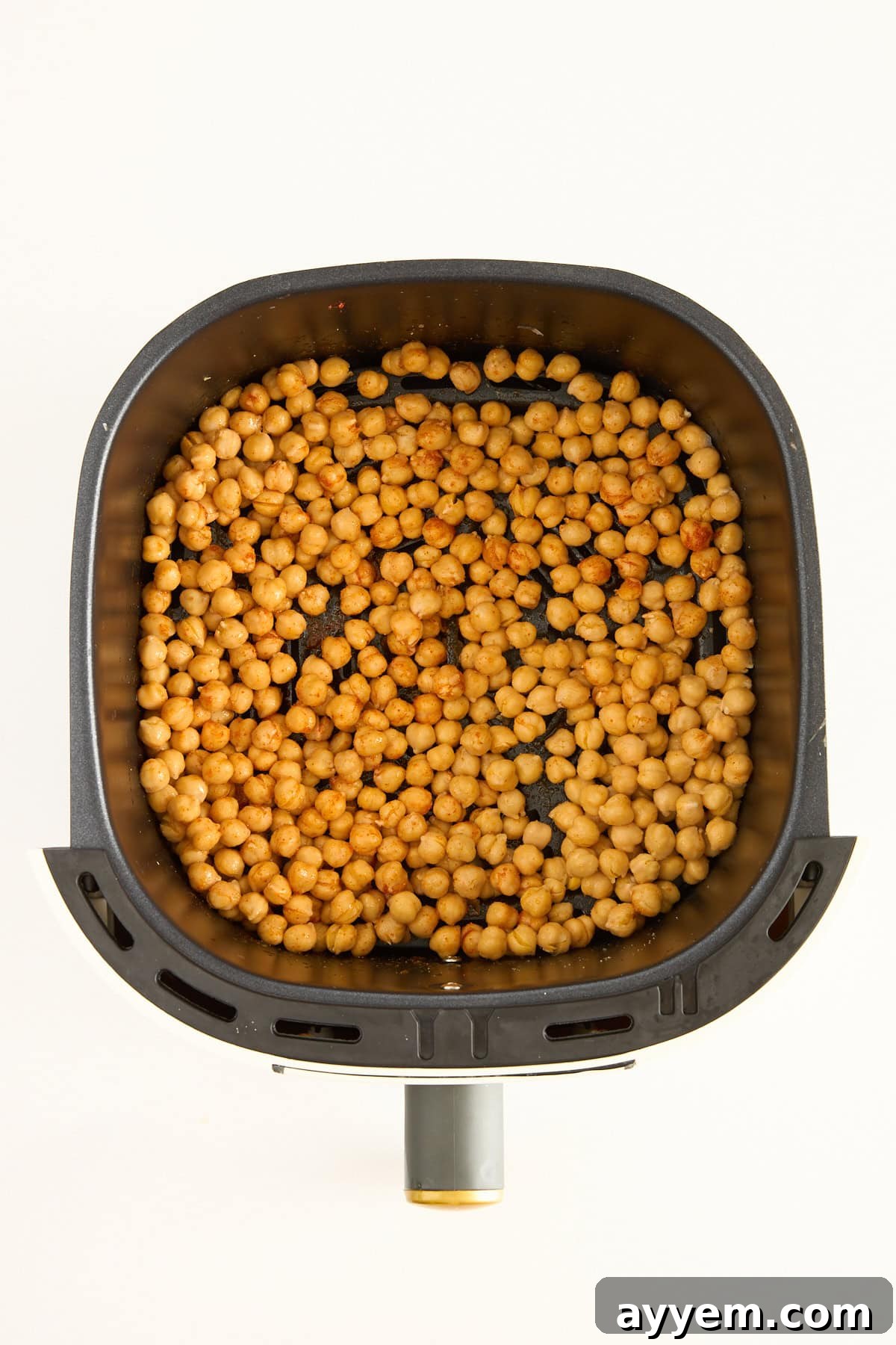 Uncooked, seasoned chickpeas spread in a single layer in an air fryer basket, ready for cooking.