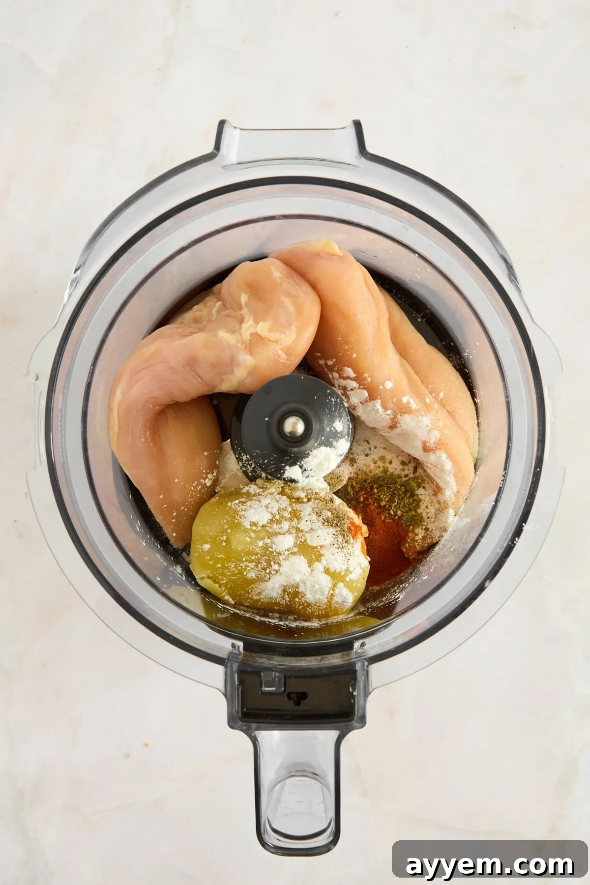 Chicken, red onion, cooked potato, and spices in a food processor, ready to be blended.