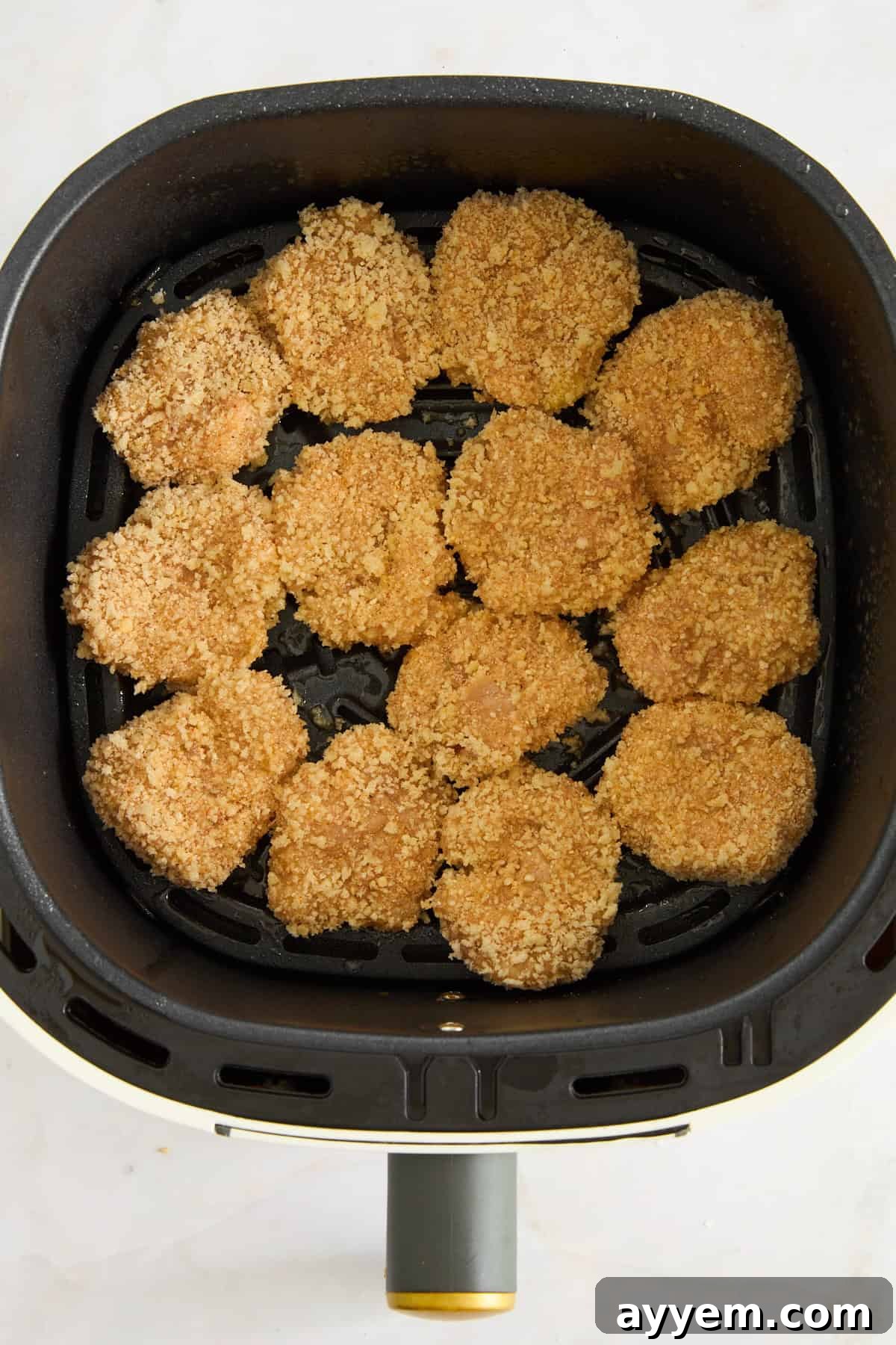 Raw chicken nuggets arranged in a single layer in an air fryer basket, ready for cooking.