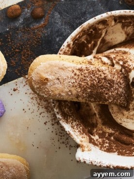 A bowl of tiramisu dip surrounded by ladyfingers and cookies.