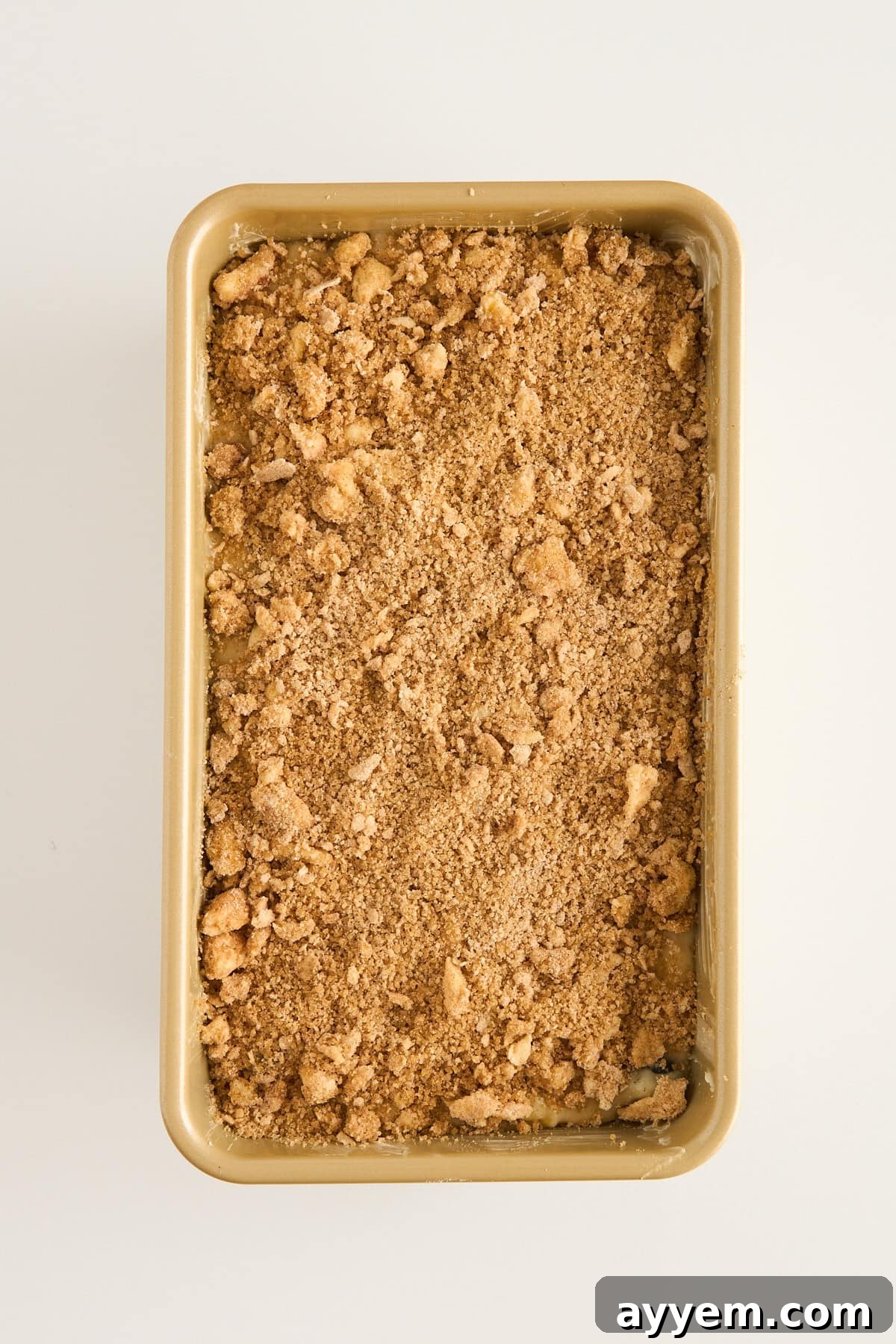 Mouthwatering Banana Blueberry Bread, Streusel Crowned 6 Rectangular baking pan filled with an even layer of crumbly, brown streusel topping on an off-white background.