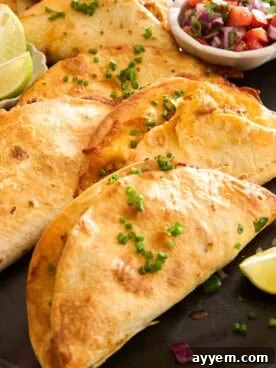 A close-up of crispy tacos filled with melted cheese, garnished with chopped chives, and served with lime wedges and a small bowl of salsa on the side.